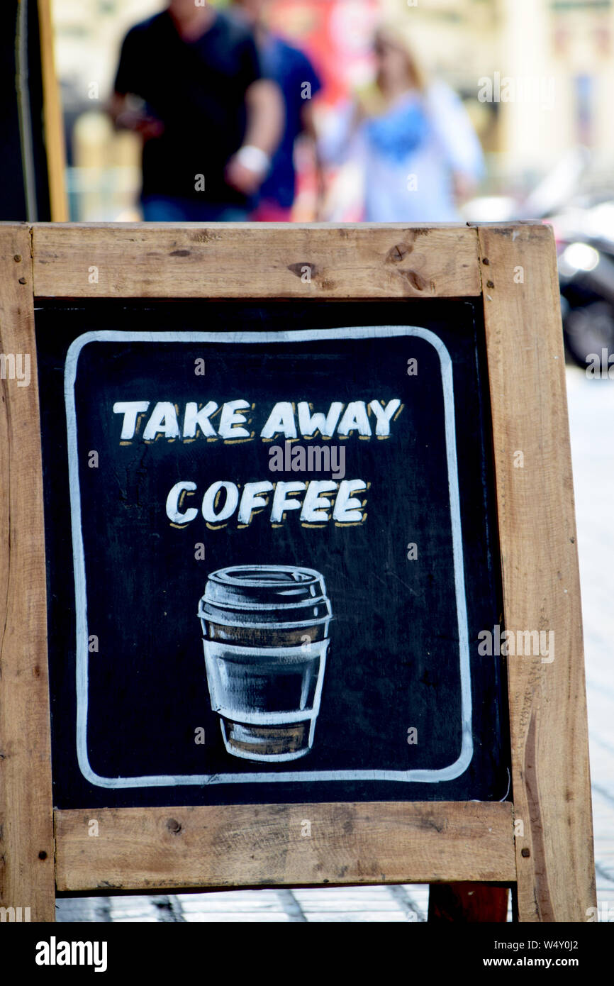 Old-fashion sidewalk sandwich board sign on the pavement with the message Take Away Coffee. Unidentifiable people in the background Stock Photo