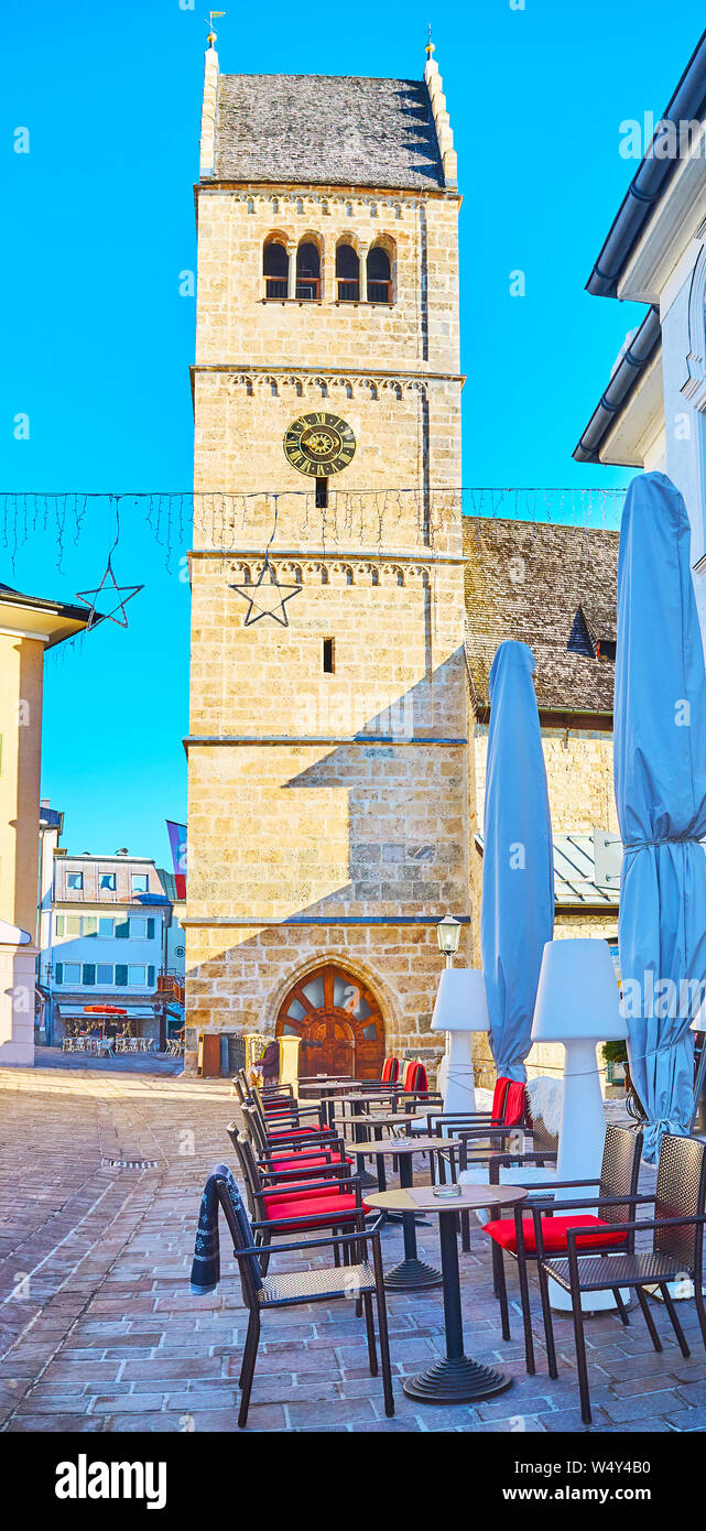 The line of small tables of outdoor cafe at the medieval bell tower of St Hippolyt Parish Church (Pfarrkirche), Zell am See, Austria Stock Photo