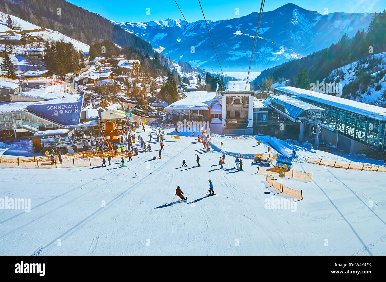 ZELL AM SEE, AUSTRIA - FEBRUARY 28, 2019: Exciting journey on modern cable car with a view on its lower station, skiers on Shcmitten mount pistes, Zel Stock Photo