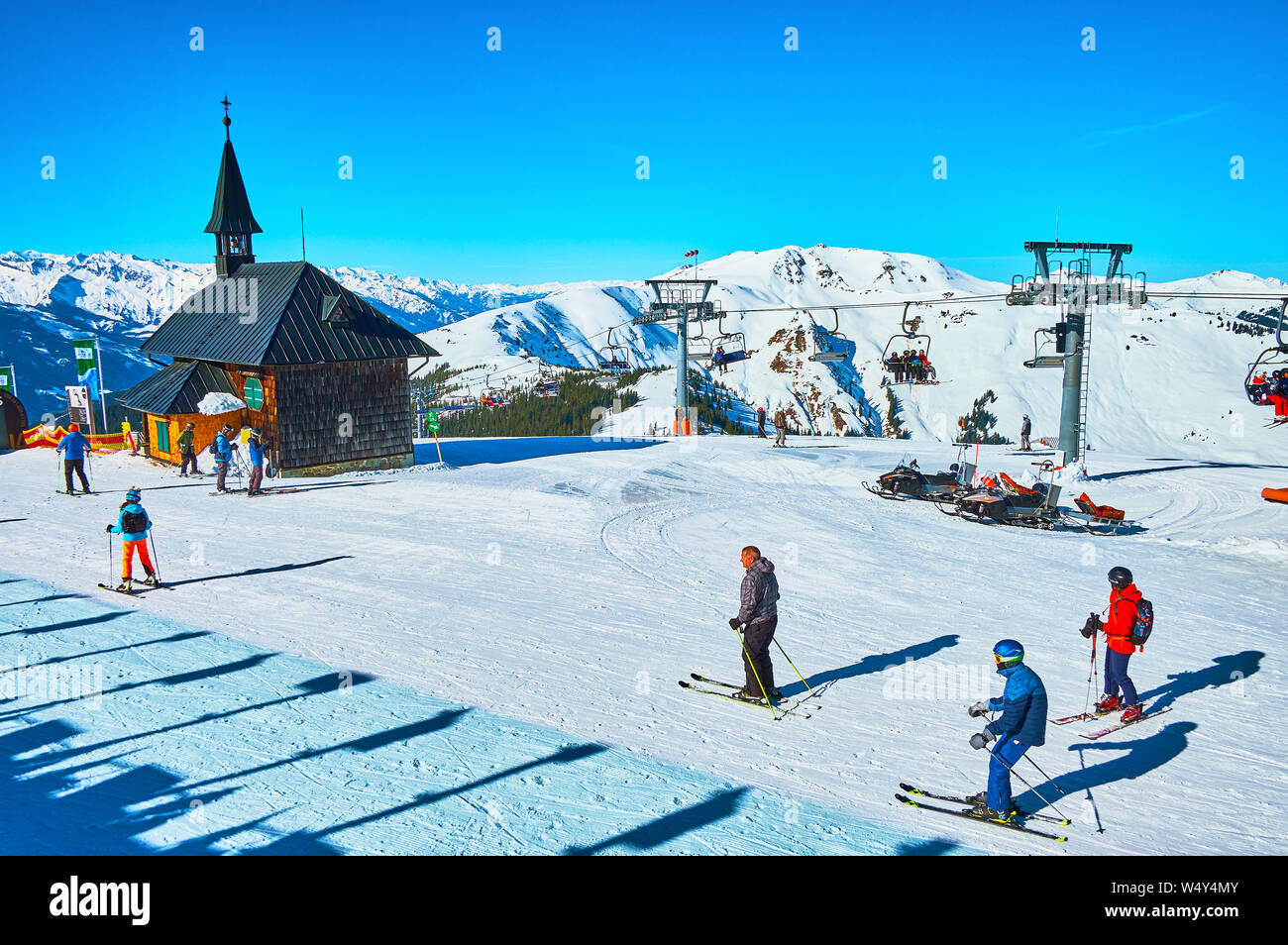 ZELL AM SEE, AUSTRIA - FEBRUARY 28, 2019: The skiers skate from the chairlift to the Schmitten mount pistes along the old wooden Elisabeth chapel, on Stock Photo