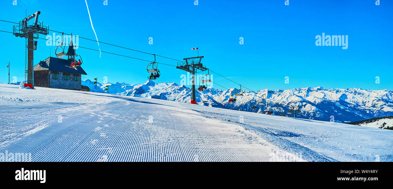 Panorama of Schmittenhohe mountain top with perfect corduroy ski piste, Kapellenbahn chairlift, small Elisabeth chapel and Alpine range on background, Stock Photo