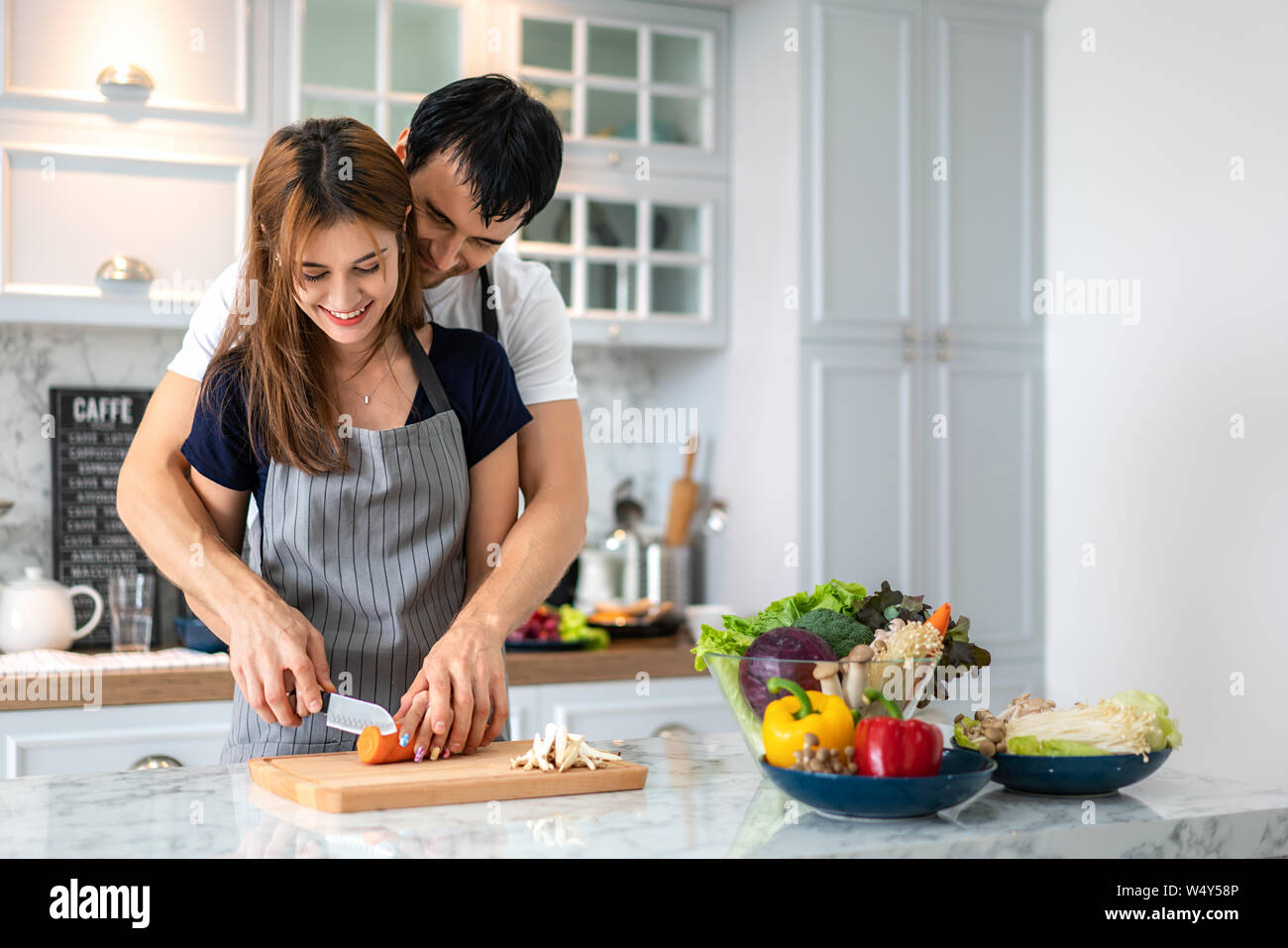 Lovely young couple preparing healthy meal in the modern kitchen. Man hugging woman romantic in morning at kitchen. Stock Photo