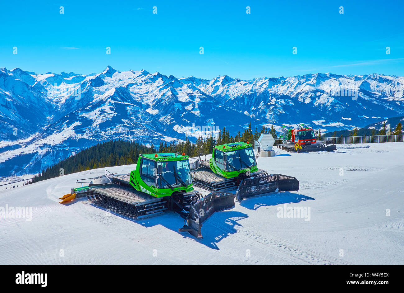 ZELL AM SEE, AUSTRIA - FEBRUARY 28, 2019: Parked snow grooming vehicles on the slope of Schmitten mount with scenic Alpine scenery and Kitzsteinhorn m Stock Photo