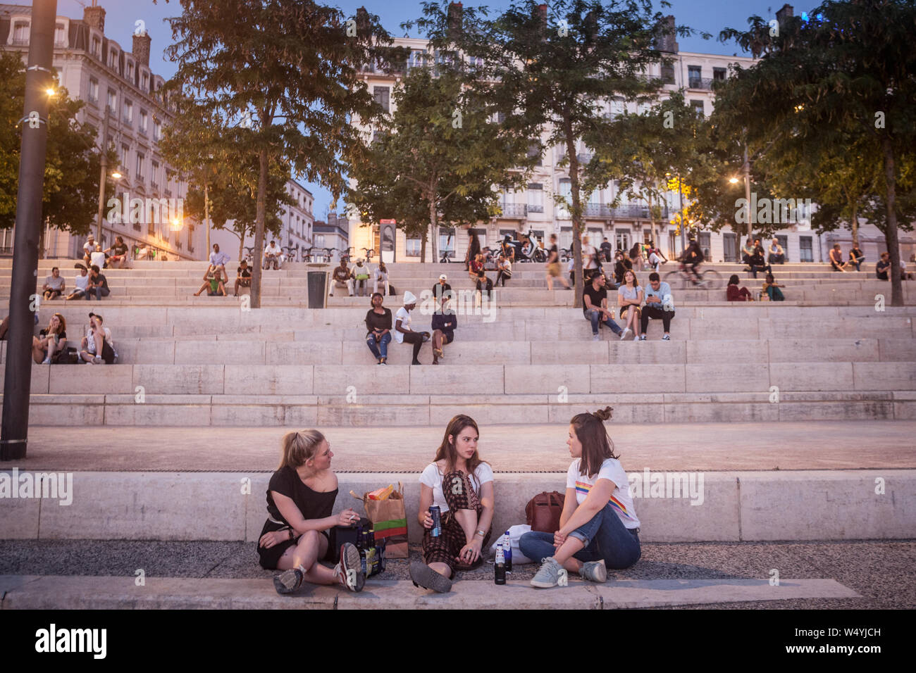 LYON, FRANCE - JULY 18, 2019: French people, mainly women and girls sitting on the riverbank of the Rhone (quais) in the evening while people are gath Stock Photo