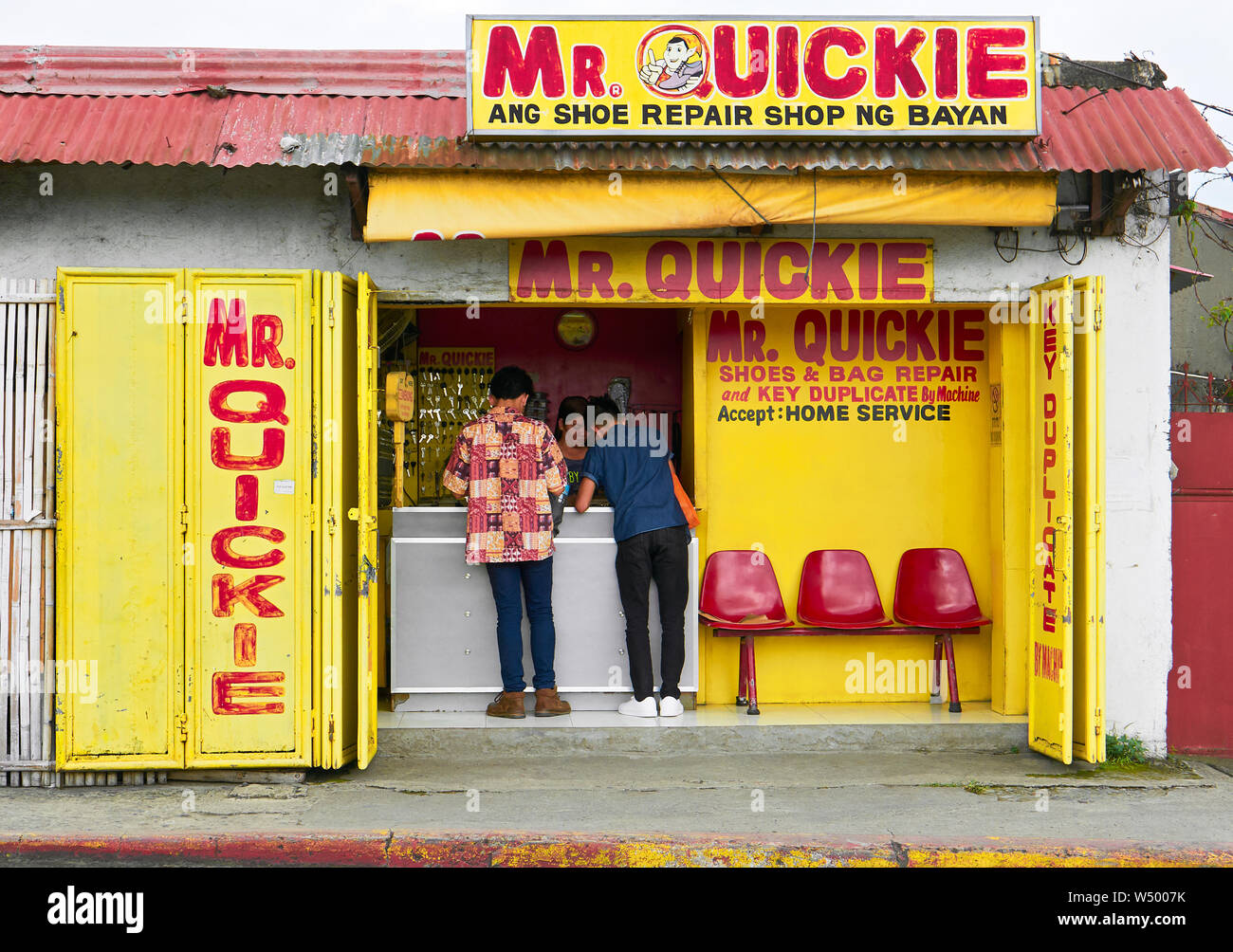Roxas City, Capiz Province, Philippines: Young customers in a colorful Mr. Quickie shoe and bag repair and key duplicate shop Stock Photo