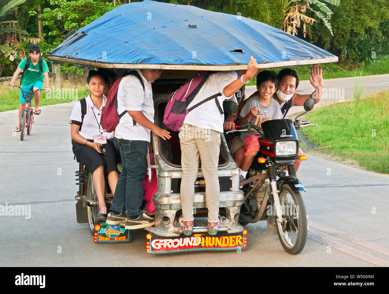 Cuartero, Capiz Province, Philippines: Young students riding home on a typical tricycle with a big roof, the driver waving Stock Photo