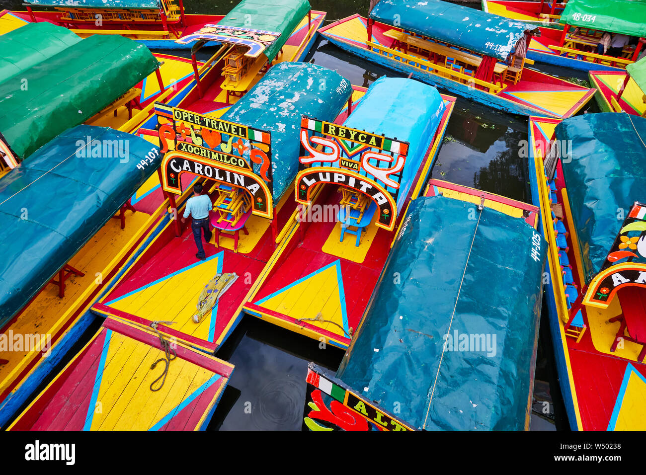 Xochimilco, Mexico City, June 25, 2019 - Trajineras moored in Nativitas Embarcadero with one man on the boat. Group of boats in Xochimilco canal. Stock Photo