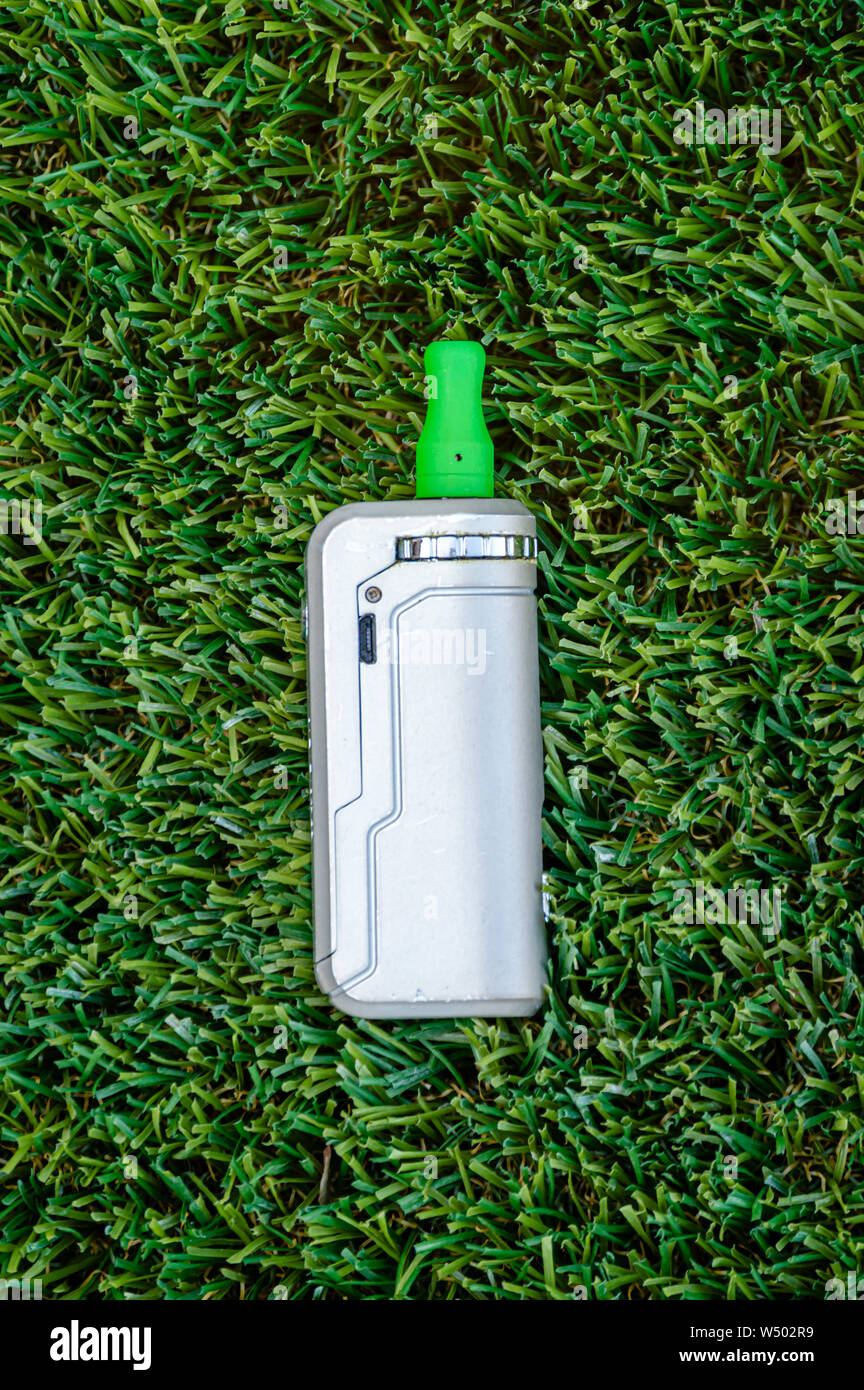 Isolated vape pen with THC CBD oil vape juice cartridge on a green grass background. Stock Photo