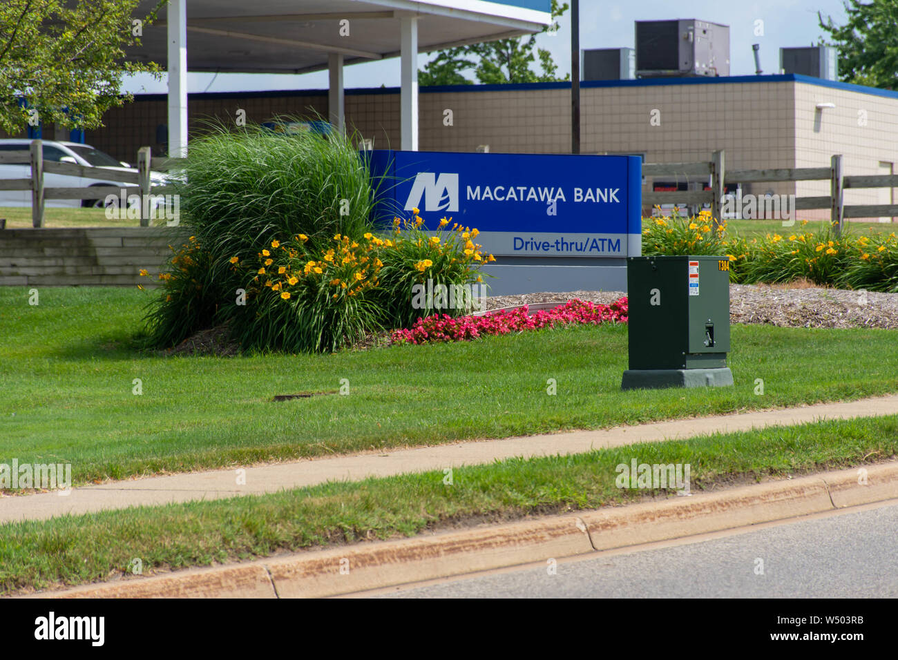 'Holland, Michigan/United States of America - 07/17/2019: Blue Macatawa Bank Sign with drive thru, atm and flowers on green grass and blue sky.' Stock Photo