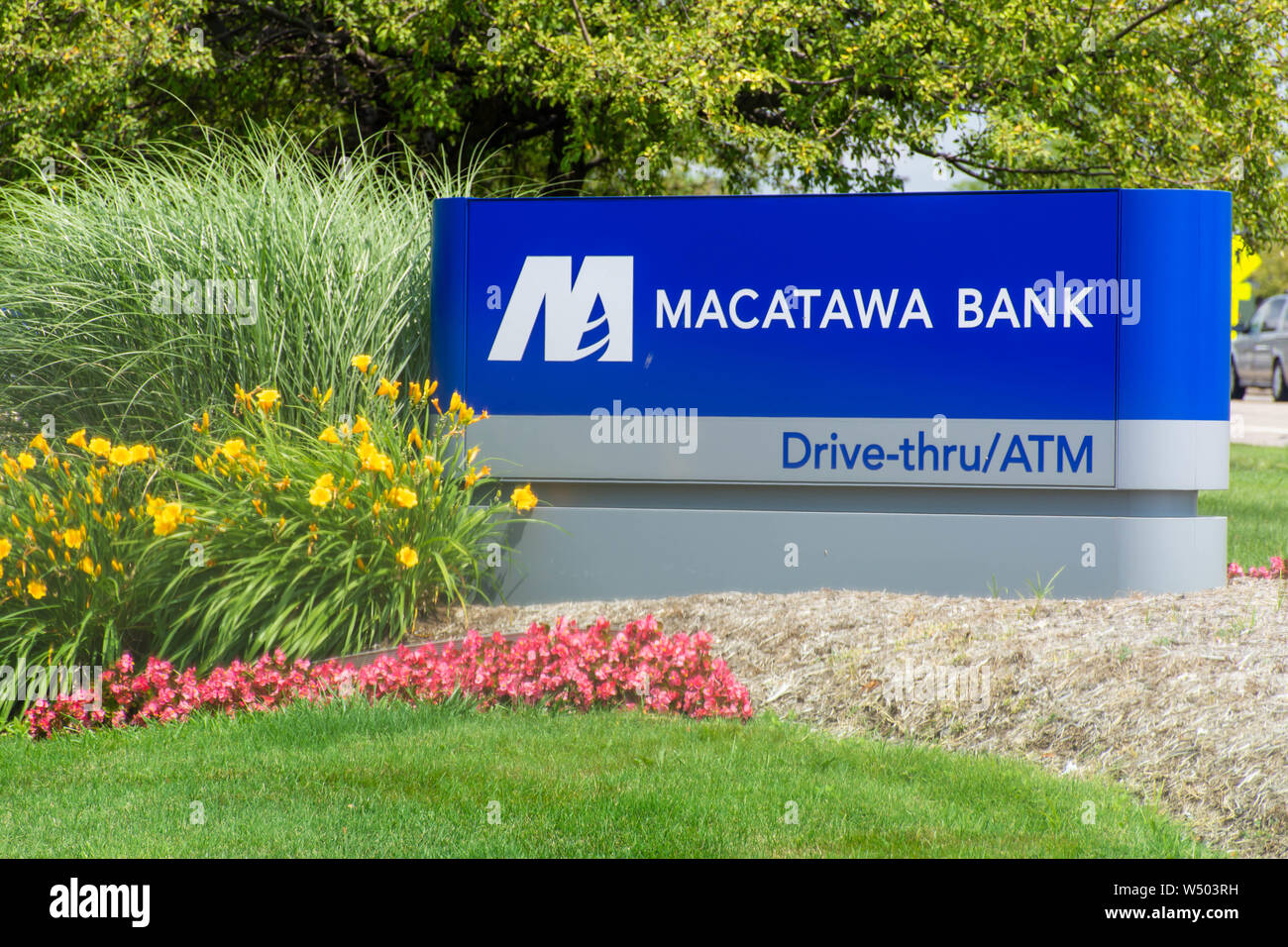 'Holland, Michigan/United States of America - 07/17/2019: Blue Macatawa Bank Sign with drive thru, atm and flowers on green grass and blue sky.' Stock Photo
