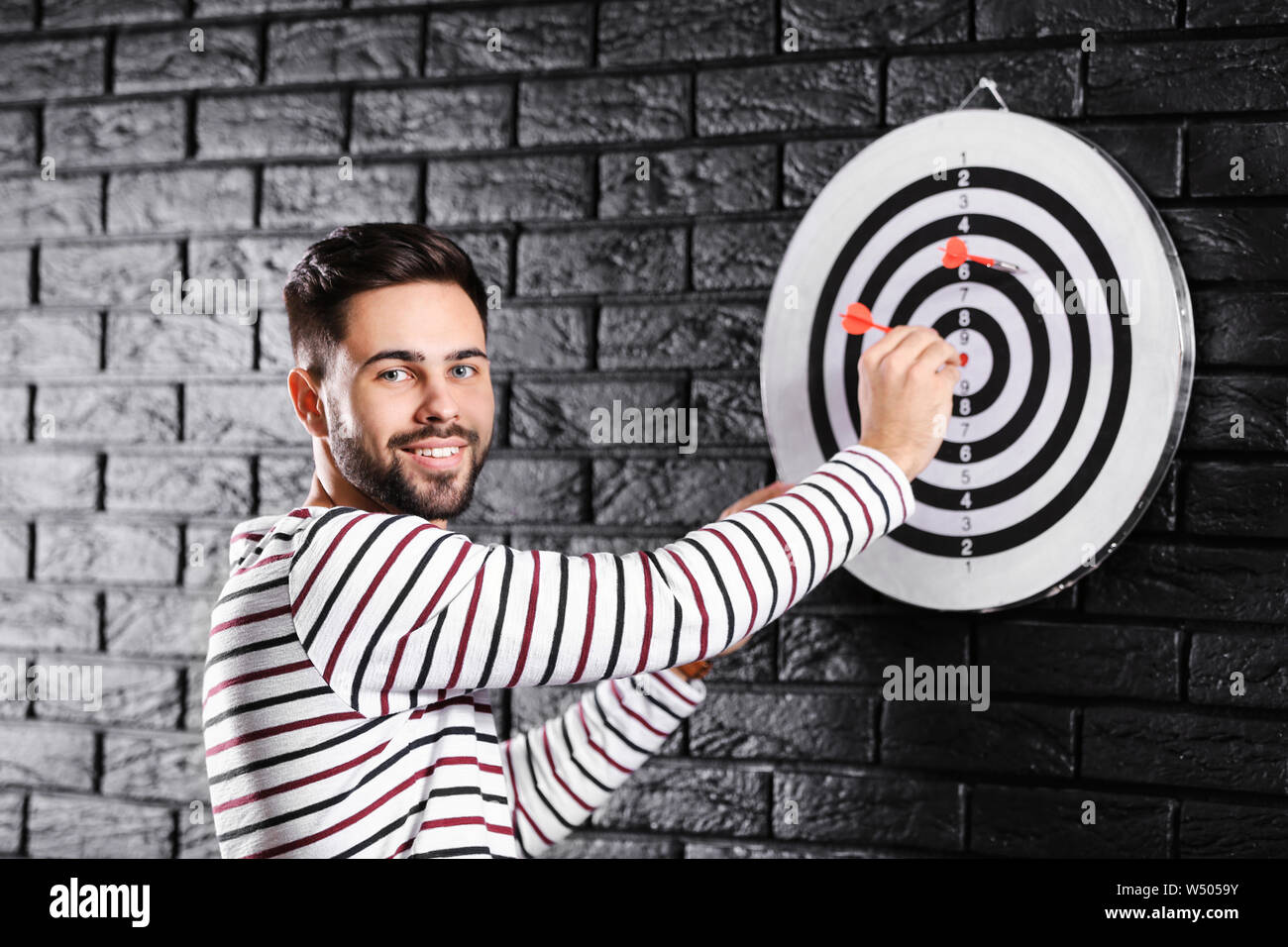 Man near dartboard on dark brick wall Stock Photo Alamy