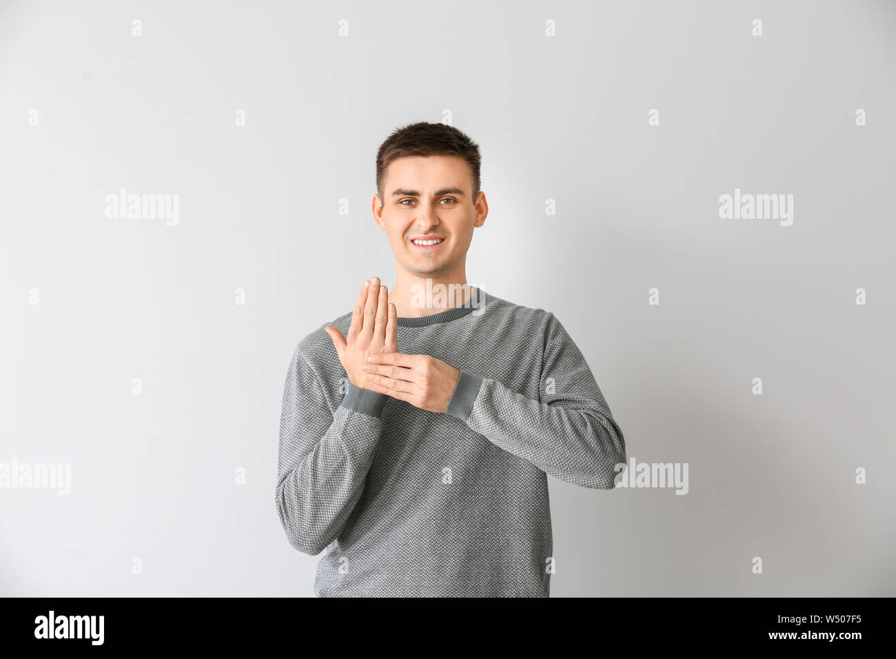 Young deaf mute man using sign language on light background Stock Photo
