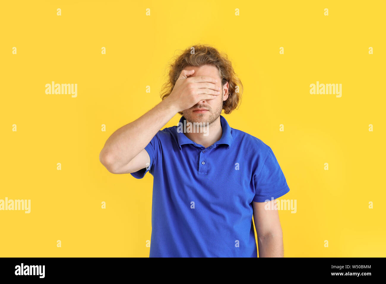 Young man covering his eyes on color background Stock Photo - Alamy