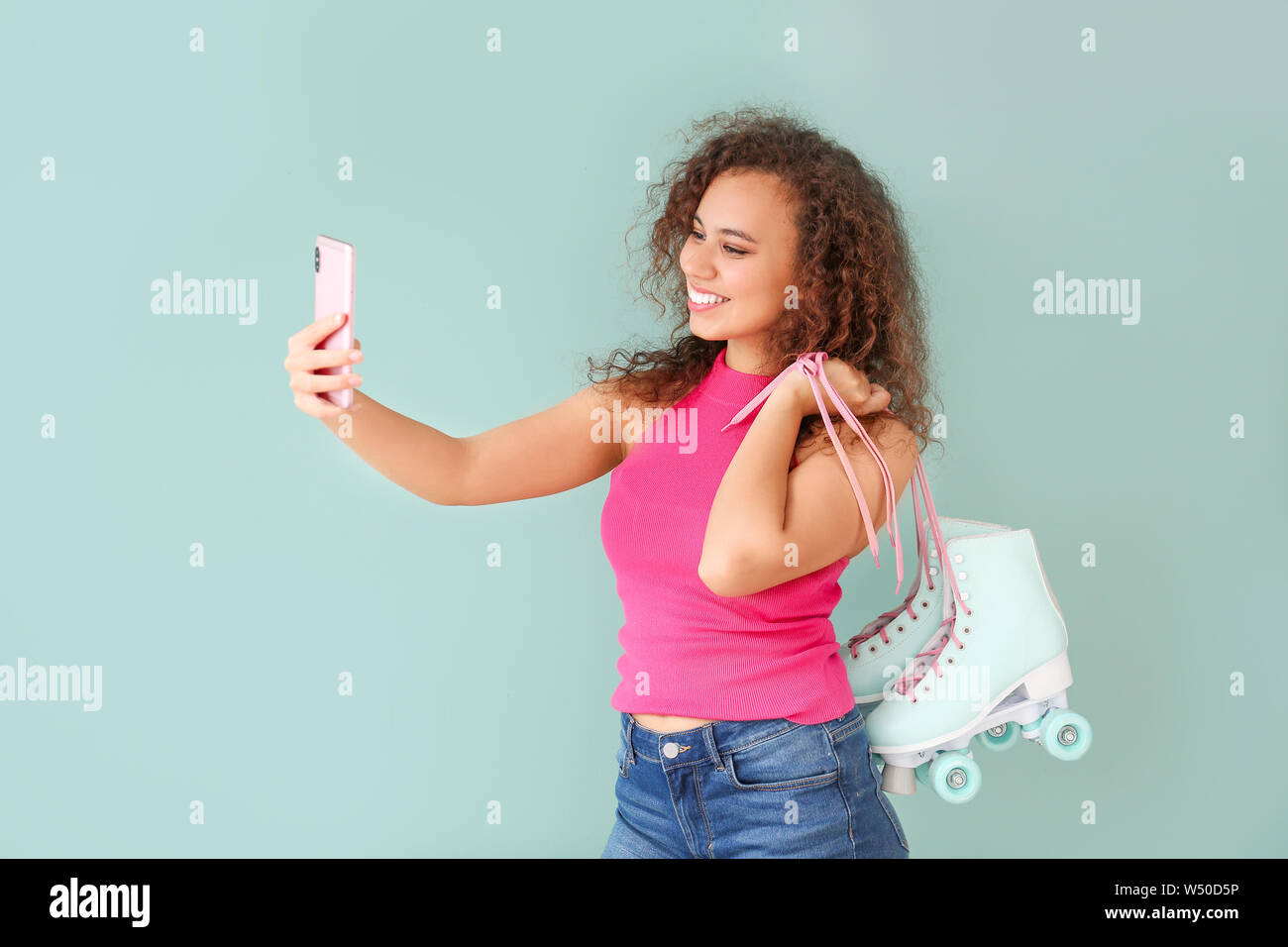 Beautiful young woman with roller skates taking selfie on color background Stock Photo