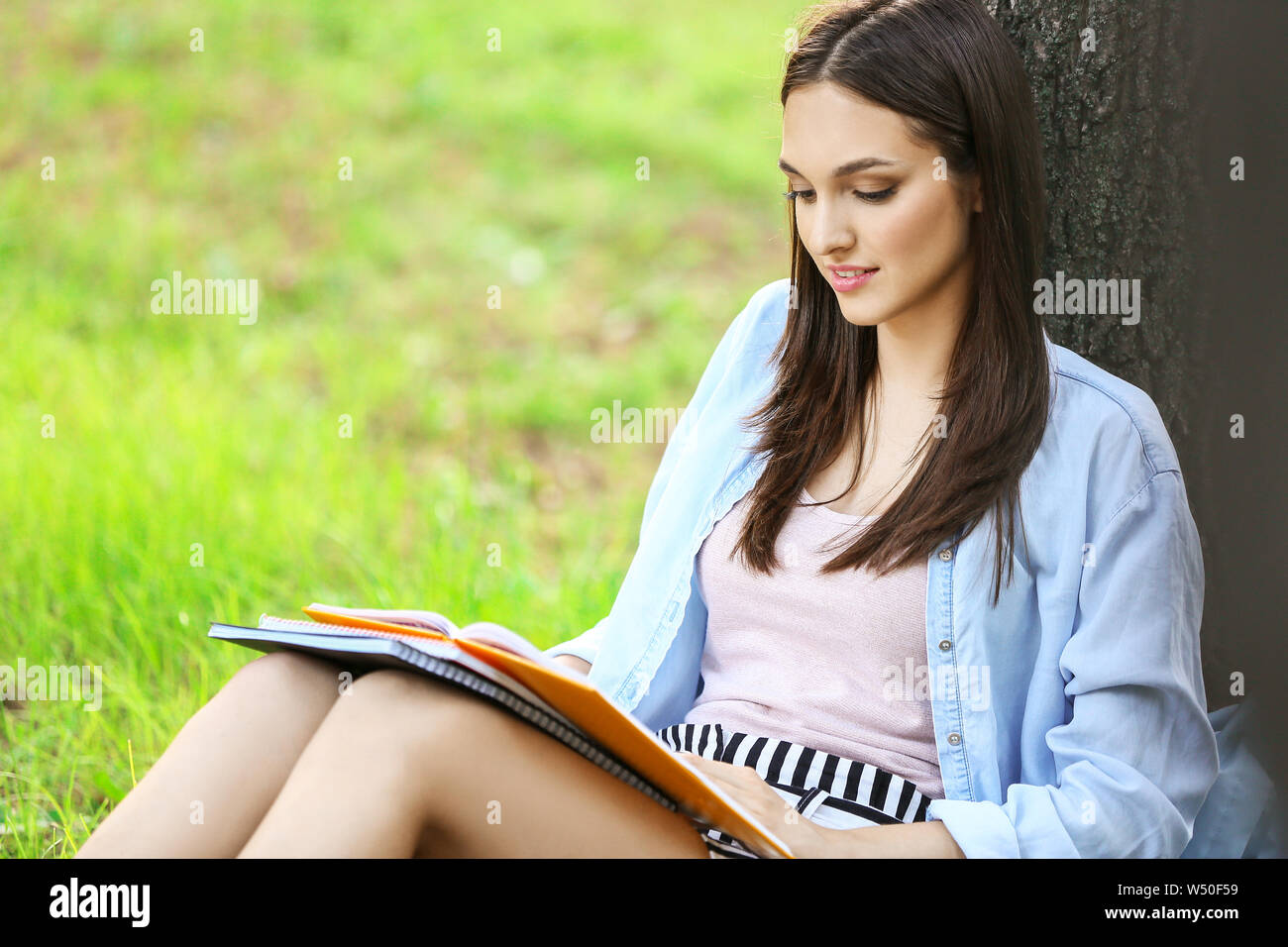 Beautiful female student sitting under tree in park Stock Photo - Alamy