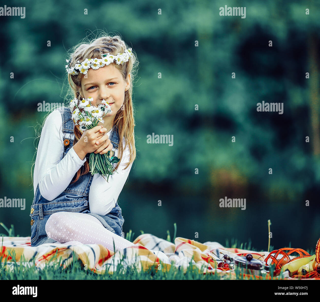 cute little girl in a wreath and a bouquet of wildflowers on a picnic ...