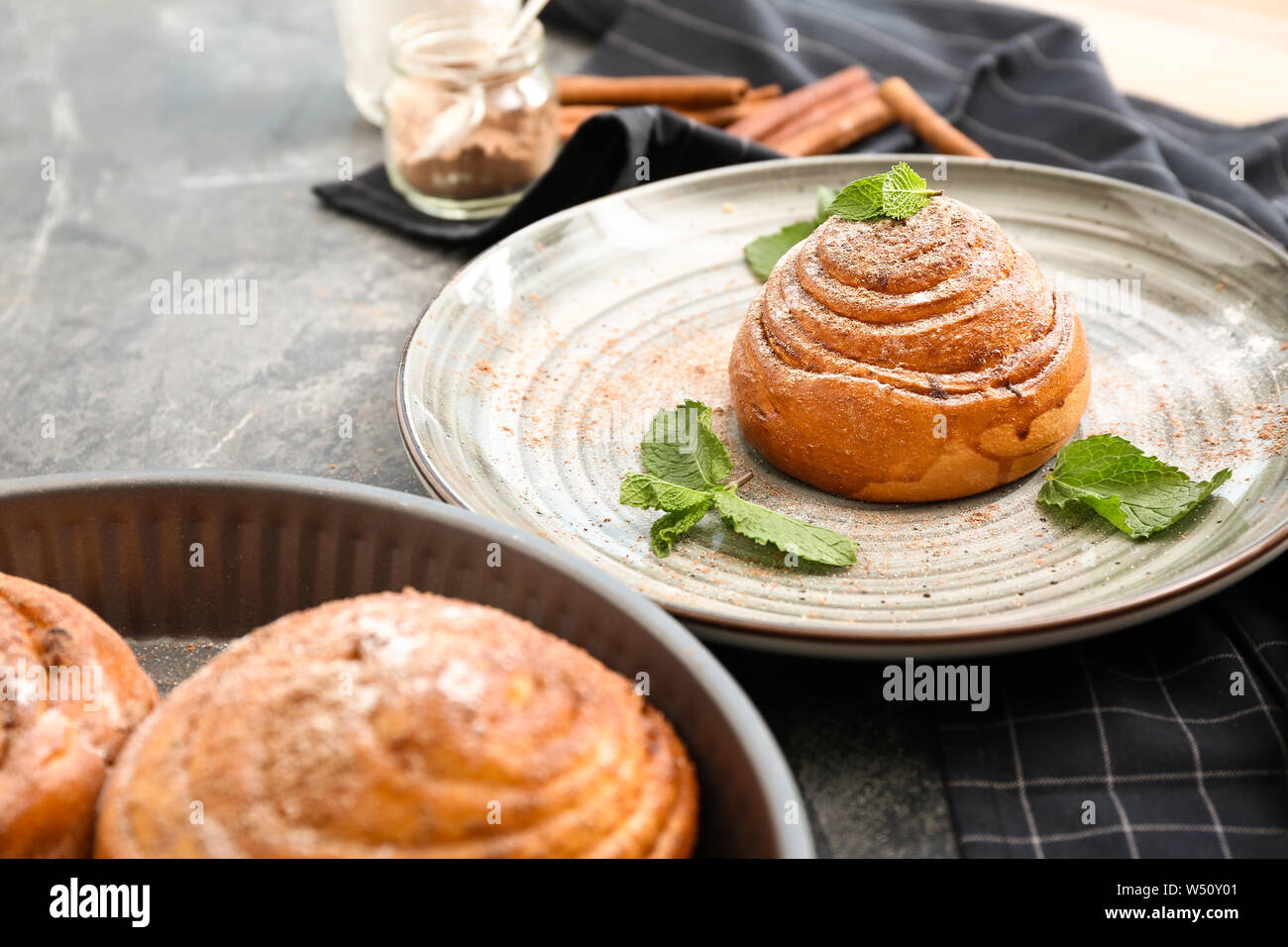 Plate with tasty cinnamon bun on grey table Stock Photo