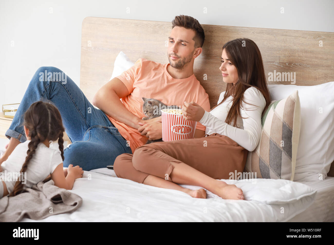 Happy family with cute cat watching TV on bed at home Stock Photo