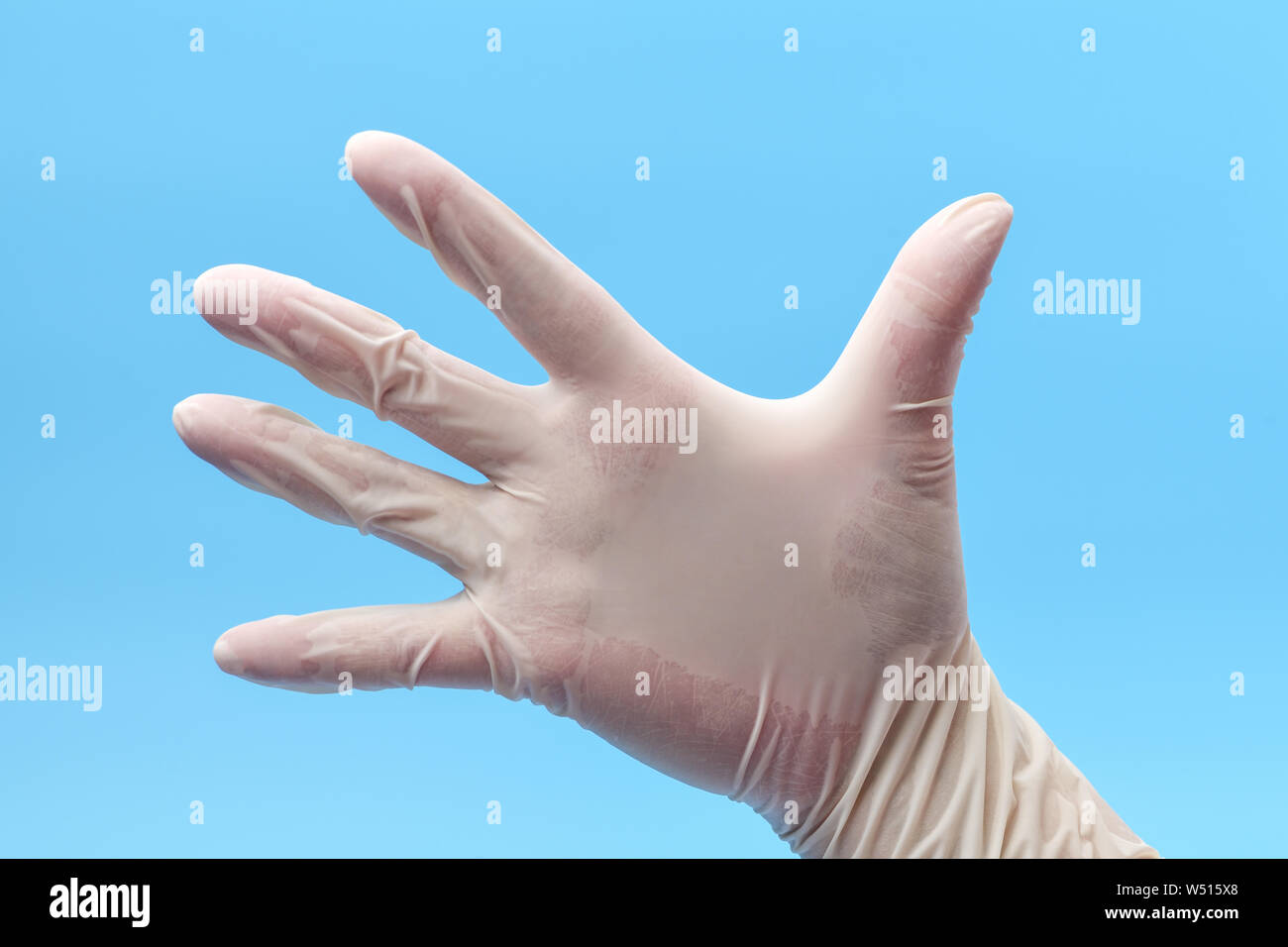 Hand Wearing Protective or Surgical Gloves on a Blue Background. Hand in white medical gloves , in position open palm. Medical background. Stock Photo