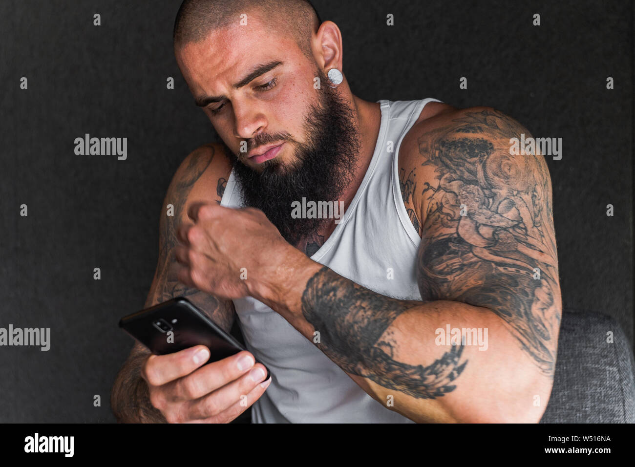 Handsome man with tattoos and beard in white t-shirt looking at smartphone  Stock Photo - Alamy