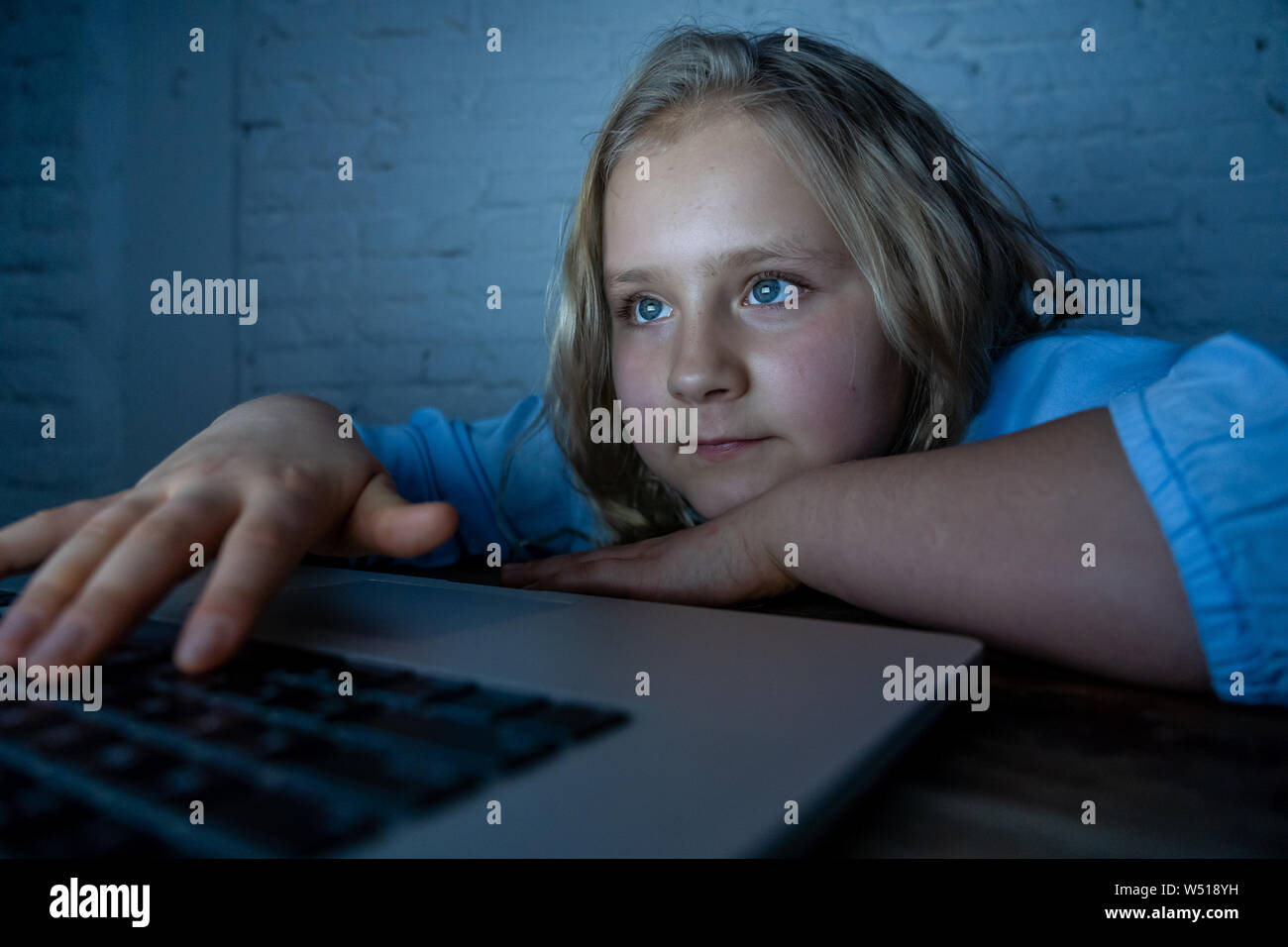 Cute schoolgirl child playing and surfing online late at night. Child addicted to internet games and social media can´t sleep hooked on laptop. Digita Stock Photo