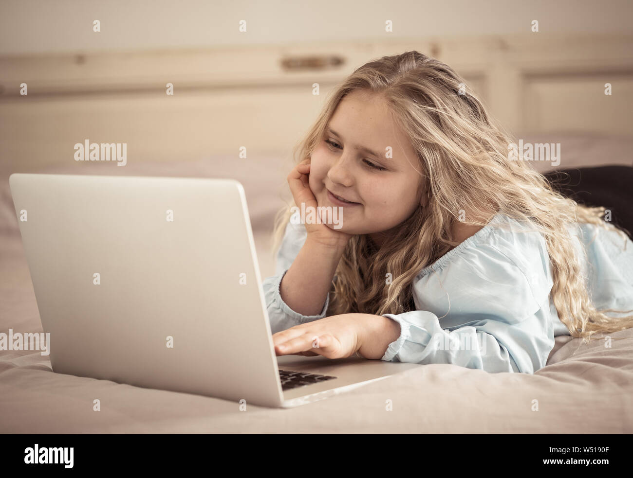 Beautiful cute happy blonde girl playing and surfing the internet on  laptop. Child watching cartoon or video on laptop on the bed at home.  Digital tec Stock Photo - Alamy