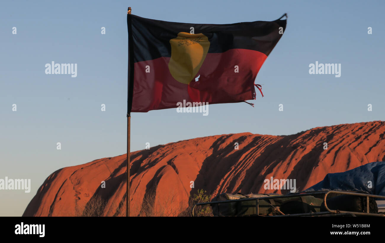 The Aboriginal flag flies in front ofUluru or Ayers Rock in Central Australia. The huge sandstone monolith is sacred to indigenous Australians. Stock Photo