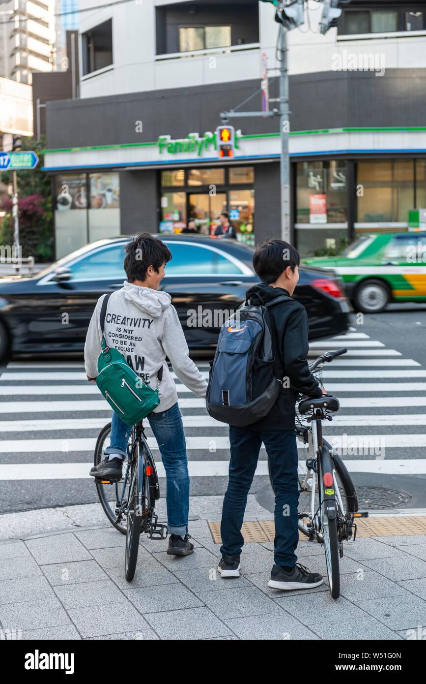 Two teenagers with bicycles waiting at a traffic light with zebra crossing, Tokyo, Japan Stock Photo