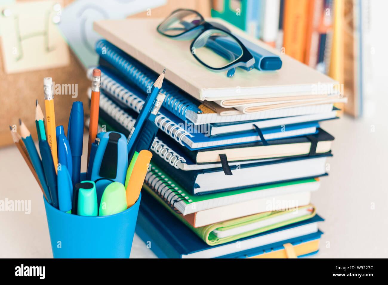 Back to school background. Stationery accessories – notebooks piles, plastic holder pencils, pens, markers, stickers, notepads, glasses and corkboard Stock Photo