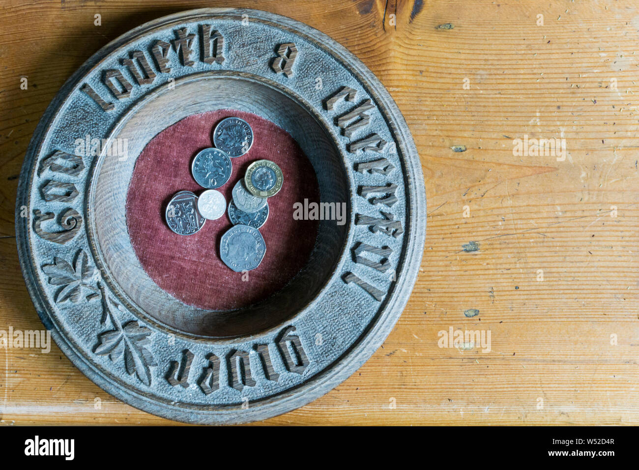 Money on a church collection plate. With 'God Loveth a Cheerful Giver' carved round the side. Stock Photo
