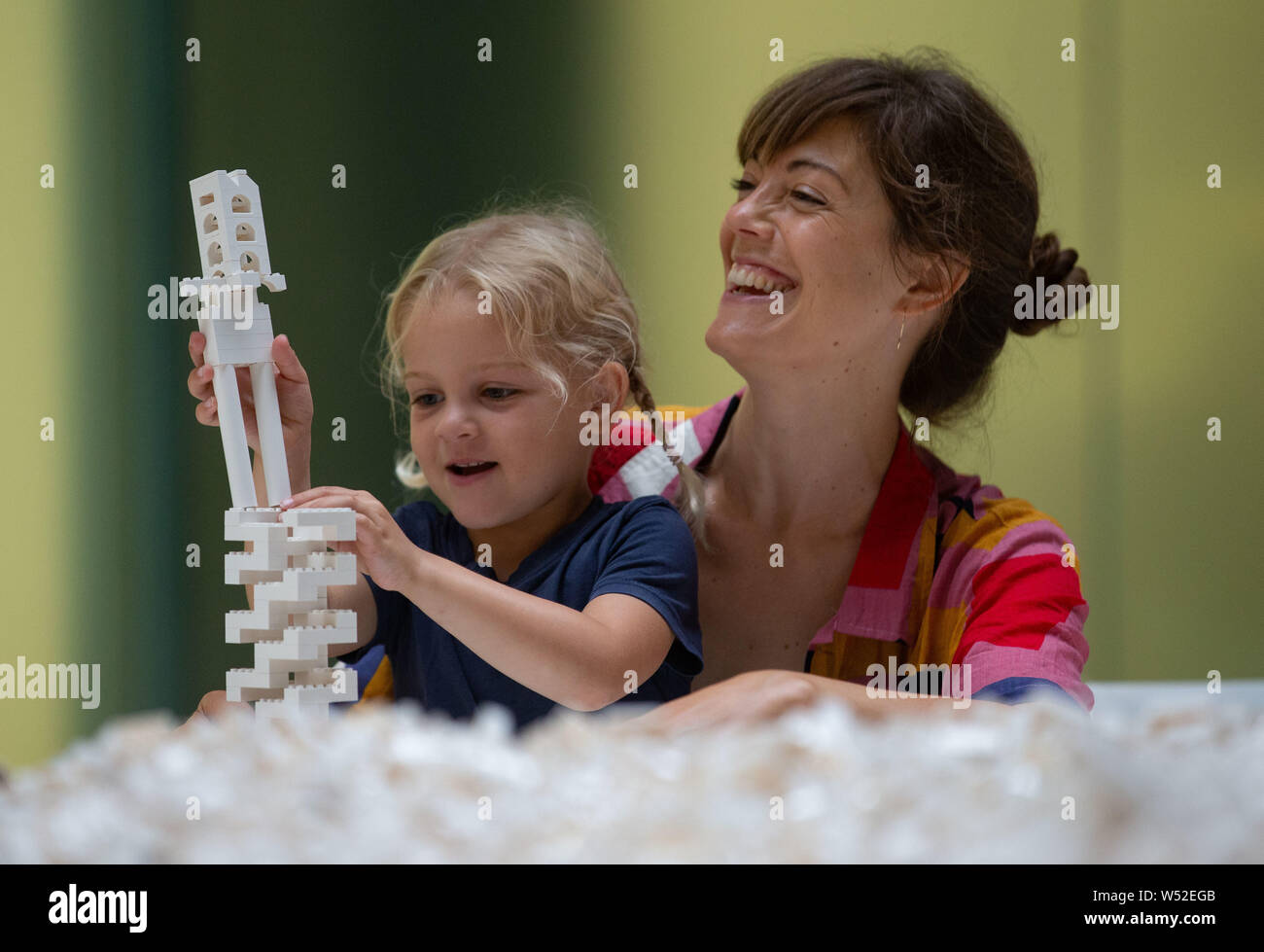 London, UK. 26th July, 2019. Ellie Cartwright helps her daughter, Margot, 4 years old. 'The cubic structural evolution project'. One Tonne of Lego bricks in Tate Modern's Turbine Hall. For three weeks this free interactive artwork will evolve and develop as visitors build thier architectural vision for a future city. Credit: Tommy London/Alamy Live News Stock Photo