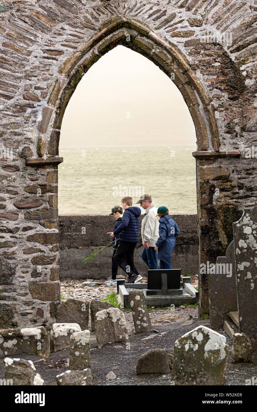 Family group passing through stone archway of ruined abbey in Ballinskelligs, County Kerry, Ireland Stock Photo