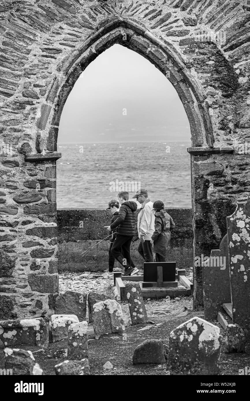 Family group passing through stone archway of ruined abbey in Ballinskelligs, County Kerry, Ireland Stock Photo