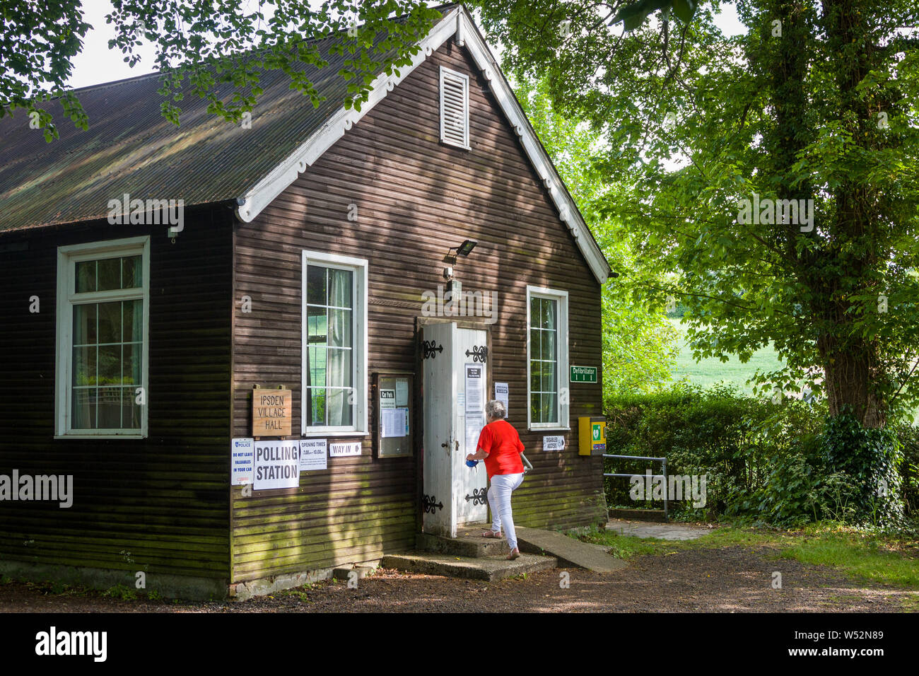 A woman in a bright red top goes to vote in the Polling Station in the village hall in Ipsden, Oxfordshire Stock Photo