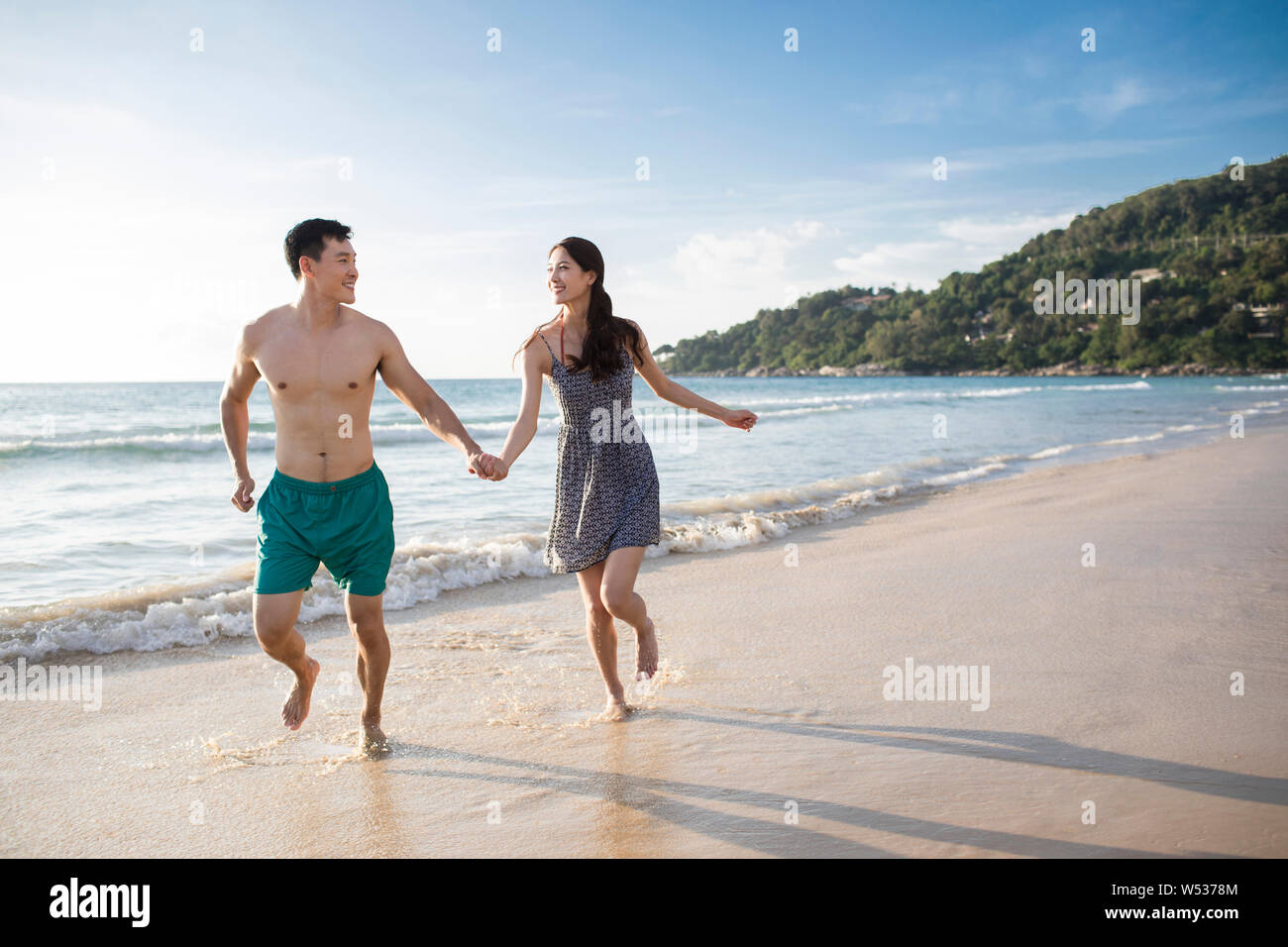 Happy young couple running on beach Stock Photo - Alamy
