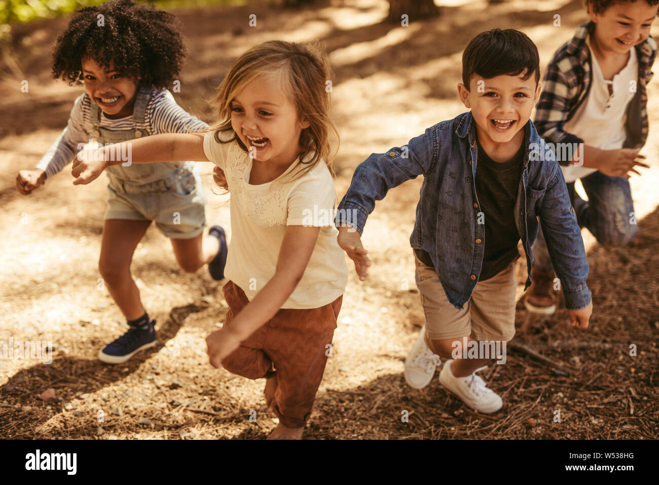 Adorable kids running up hill in a park. Group of children playing together in forest. Stock Photo