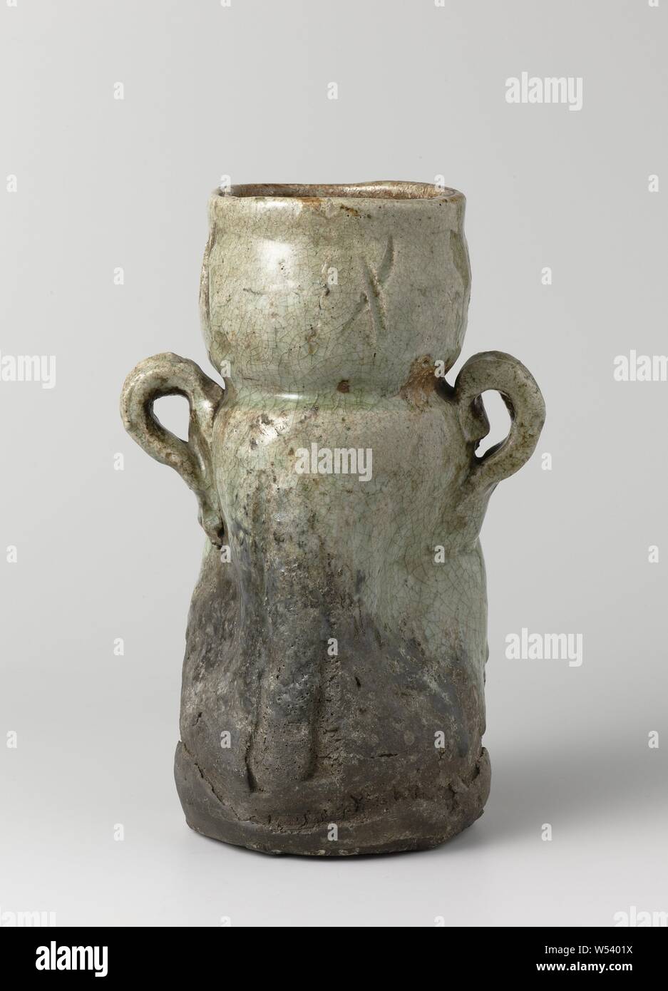 Vase with a green glaze and two handles, Vase of stoneware with two ears on the shoulder, partially covered with a celadon green glaze. The abdomen is dented and four times an engraved cross on the neck. The lower part of the vase is unglazed. Old trader's label on the bottom with 'N.V. Hammer - Far Eastern Art New York / 440 '. I go., anonymous, Japan, c. 1600 - c. 1699, Edo-period (1600-1868), stoneware, glaze, vitrification, h 26.7 cm d 10.5 cm d 14.1 cm d 11.8 cm l 17.5 cm Stock Photo