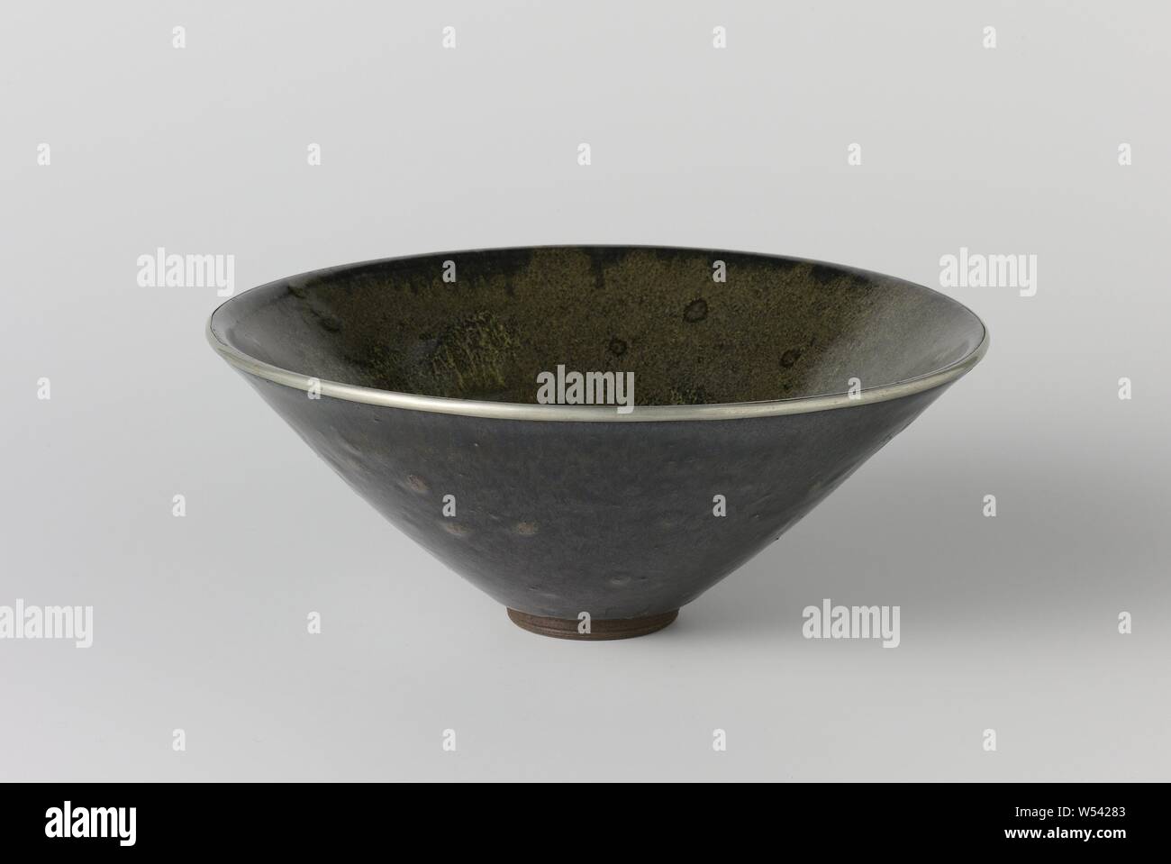 Teabowl with a green black glaze, Stoneware tea bowl, partially covered with a green-black glaze. The edge is enclosed in a metal band. The bottom and the foot ring are unglazed. Imitation of a Chinese temmoku. Seto., anonymous, Japan, c. 1500 - c. 1699, Edo-period (1600-1868), stoneware, glaze, rand, vitrification, h 8.7 cm d 22.2 cm d 4.9 cm Stock Photo