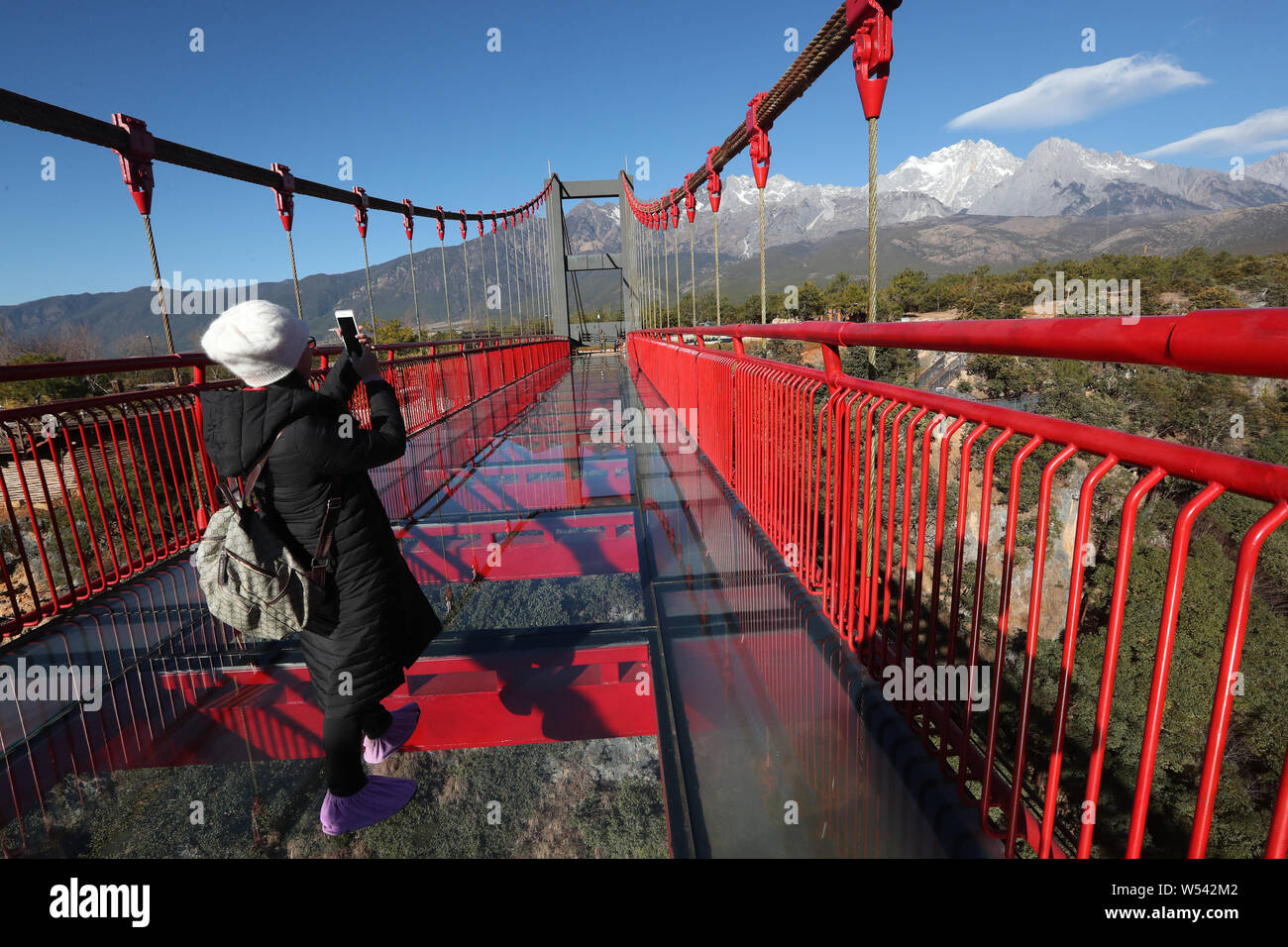 Visitors pose for photos on a glass-bottomed suspension bridge spanning over a canyon at the Jade Dragon Snow Mountain scenic area in Lijiang city, so Stock Photo
