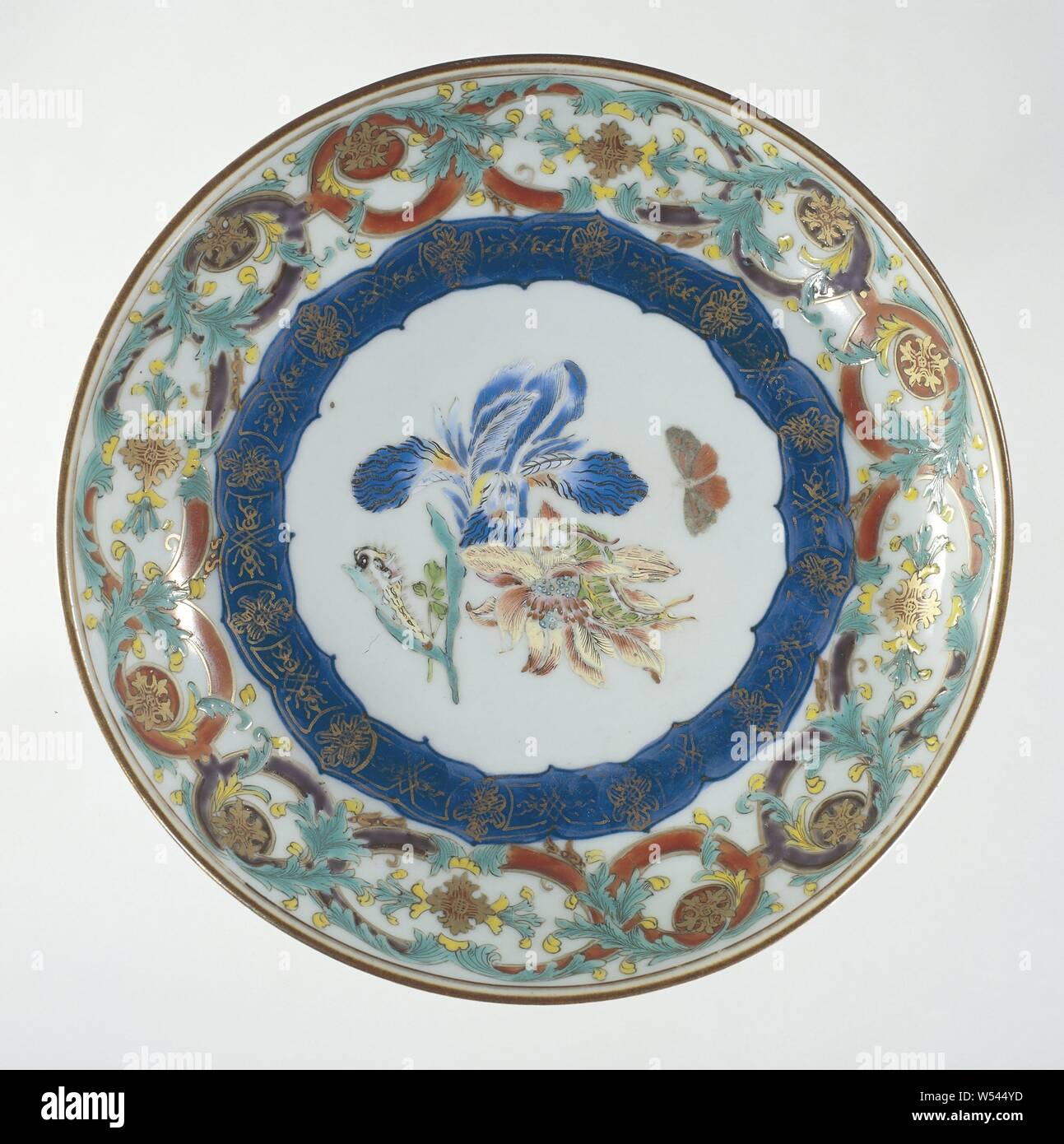 Saucer-dish with flowers, butterfly and ornamental borders, Porcelain dish with round wall, painted in underglaze blue and on the glaze in blue, red, pink, green, yellow, black and gold. On the flat two flower branches (iris, anemone) on which two caterpillars, next to it a flying butterfly, around it a decorative band in underglaze blue with gold, the wall a band with a switched pattern with leaf vines, the outer edge with a band of napkin work. European representation in enamel colors., anonymous, China, c. 1740 - c. 1750, Qing-dynasty (1644-1912) / Qianlong-period (1736-1795), porcelain Stock Photo