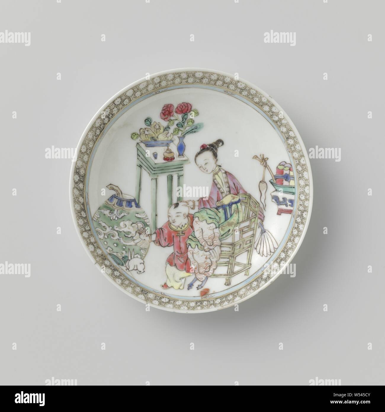 Saucer with lady, boy and precious objects, Porcelain dish, painted on the glaze in blue, pink, green, yellow, black and gold. On the shelf a lady sitting on a chair with a boy and a rabbit, around them symbols of happiness and antiques (including a vase with peacock feathers, incense burner, finger lemon, rolls), a band with napkin work on the edge. Wall has been broken. Famille rose., anonymous, China, c. 1725 - c. 1749, Qing-dynasty (1644-1912) / Yongzheng-period (1723-1735) / Qianlong-period (1736-1795), porcelain (material), glaze, gold (metal), vitrification, h 1.8 cm d 11.1 cm d 6.8 cm Stock Photo