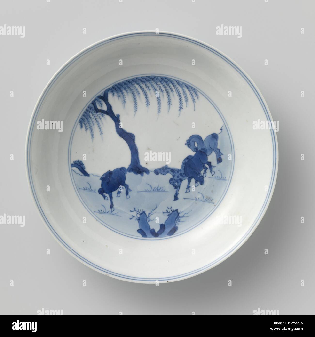 Saucer-dish with horses in a landscape, Porcelain dish with round wall, painted in underglaze blue. On the flat four horses in a landscape with rocks and a tree, the rear with four galloping horses in a landscape with rocks and a tree. Marked on the underside with the six-character mark of Emperor Chenghua in a double circle. Blue White., anonymous, China, c. 1680 - c. 1720, Qing-dynasty (1644-1912) / Kangxi-period (1662-1722), porcelain (material), glaze, cobalt (mineral), vitrification, h 3.4 cm d 16.9 cm d 9.7 cm Stock Photo