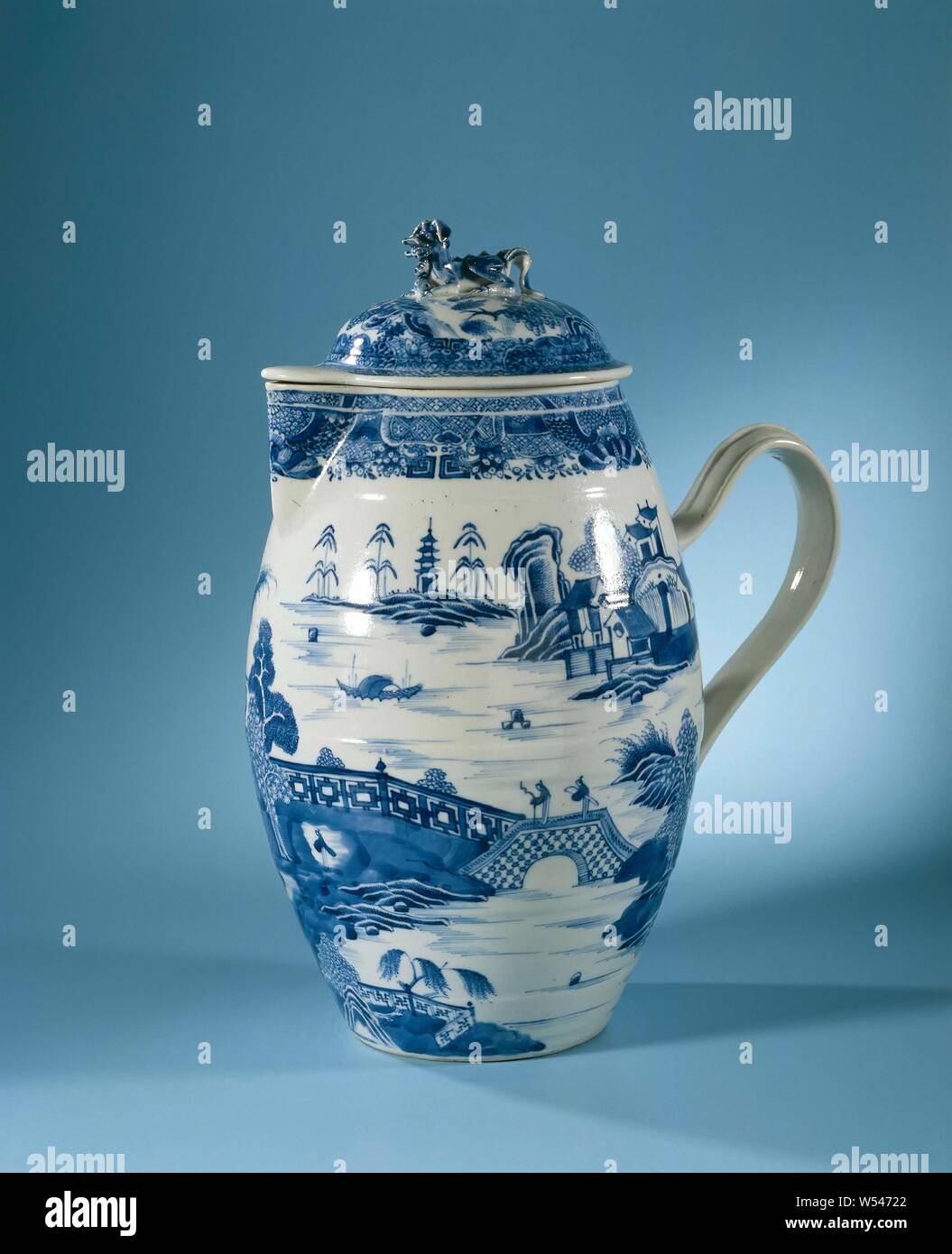 Pitcher with a riverlandscape with large pavilion and figures, Jug with porcelain lid with a barrel-shaped belly, triangular spout and rim, painted in underglaze blue. On the wall of the jug a continuous river landscape with pavilions, mountains, trees, people and a boat, the edge with FitzHugh strap, a branch on the ear. The lid with a river landscape with two people on a bridge, mountains and pavilions, the bud in the shape of a lion. Blue White., anonymous, China, c. 1800 - c. 1824, Qing-dynasty (1644-1912) / Jiaqing-period (1796-1820) / Daoguang-period (1821-1850), porcelain (material Stock Photo