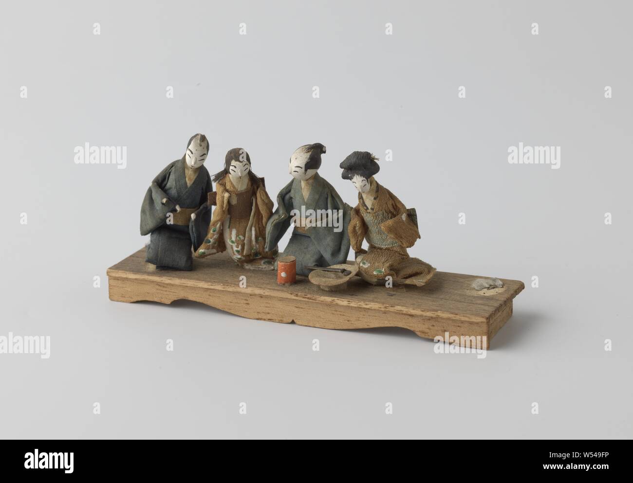 Elongated board with four squat dolls (one standing puppet is missing), Elongated board with four squat dolls and - originally - one standing in Japanese clothing. The standing doll is missing, Japan, 1900 - 2000, wood (plant material), h 6 cm × w 13.5 cm × d 4 cm Stock Photo