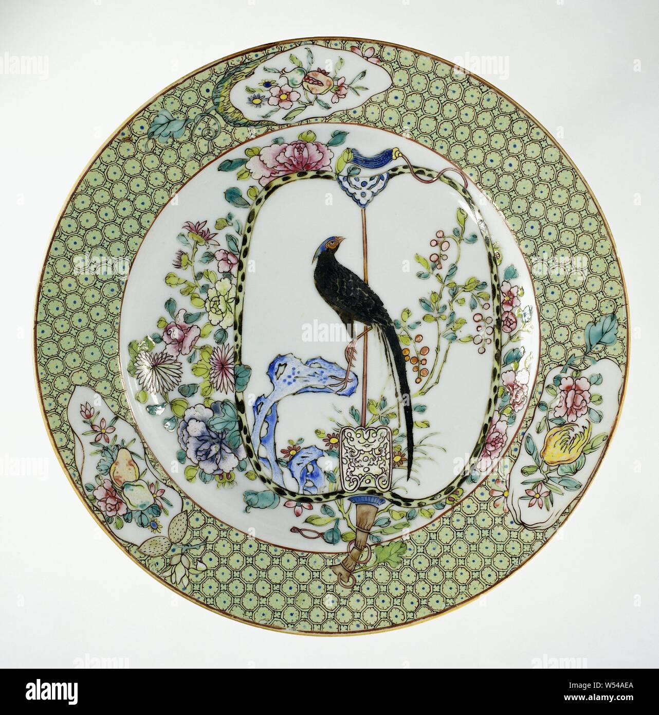 Plate with a fan decorated with a pheasant, Porcelain plate, painted on the glaze in blue, red, pink, green, yellow, black and silver. On the shelf a fan whose handle extends to the wall and edge, on the fan a pheasant on a rock with flowering plants is depicted, around the range of peony and chrysanthemum branches, on the edge napkin work interspersed with three cartouches in the form of fruits with fruit branches. Two cracks in the edge. Famille rose., anonymous, China, c. 1730 - c. 1745, Qing-dynasty (1644-1912) / Yongzheng-period (1723-1735) / Qianlong-period (1736-1795), porcelain Stock Photo