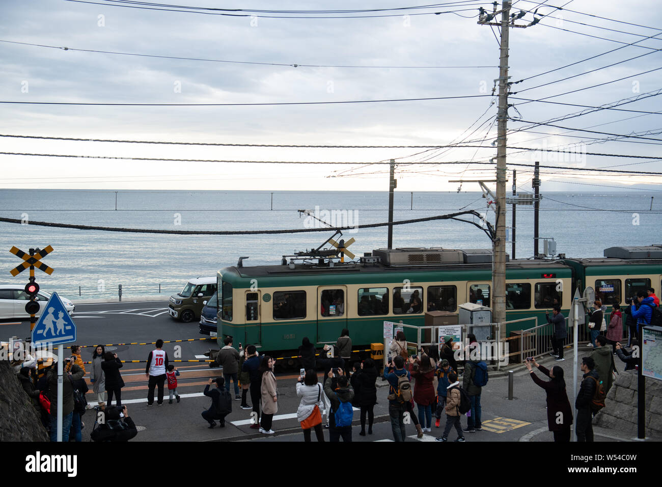 Tourists Take Photos As A Train On The Enoden Line Travels Past The Railroad Crossing Against The Skyline Of Sea Scape In Kamakura Kanagawa Japan 2 Stock Photo Alamy