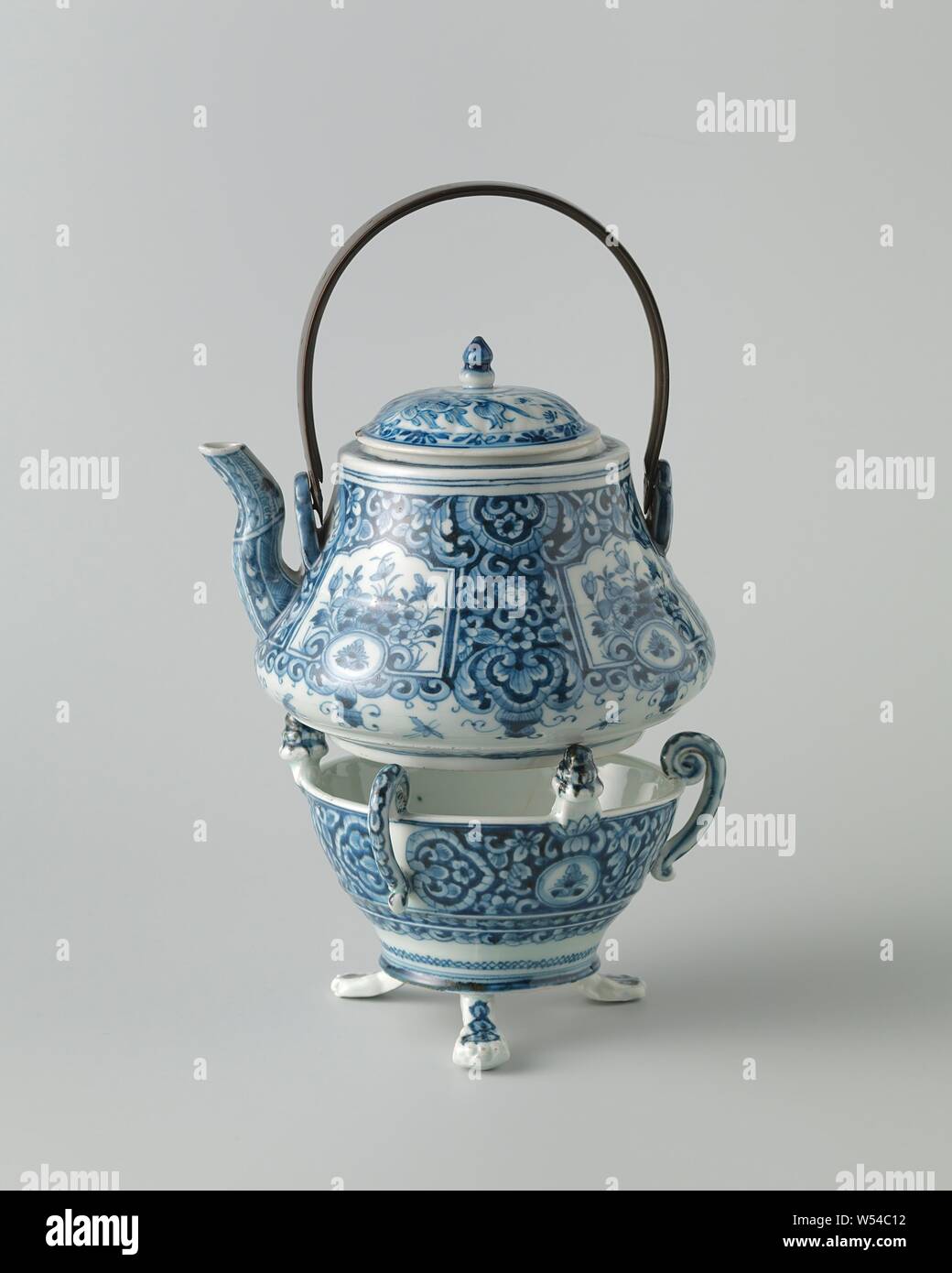 Kettle with flowering plants and foliate scrolls, Printed baluster-shaped kettle made of porcelain with an S-shaped spout and two eyes to which a whale bone handle is attached. Painted in underglaze blue. On the wall of the kettle four rectangular boxes, painted at the top, with a medallion with a flower branch at the bottom. Flowering plants in the boxes. The boxes are cut into a background of leaf vines, lambrequins and small human heads with curly hair. Blue White., anonymous, Japan, c. 1750, Edo-period (1600-1868), porcelain (material), glaze, cobalt (mineral), hengsel, vitrification, h 13 Stock Photo
