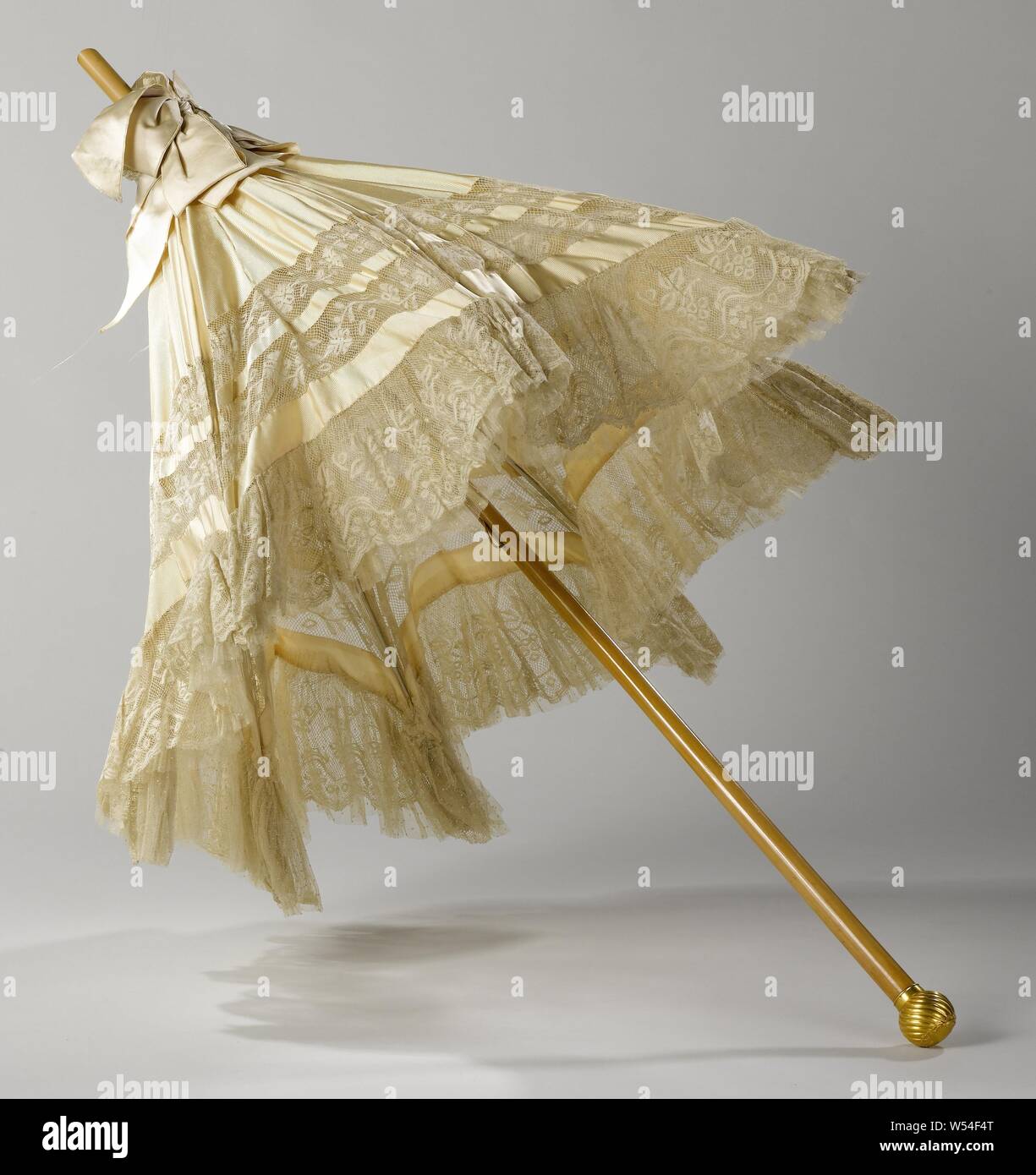 Parasol with machine-made lace Parasol with creme-colored ripping-side deck with a strip of machine-made Valenciennes lace, on light wooden stick with a twisted brass button with rocaille ornaments, Parasol with crêm-colored ripping-side deck on which a strip from the Valenciennes mechanical side. Unlined, eight lined ribs. On top a cream colored silk bow. Light-colored wooden stick with a convex, twisted brass button with rocaille ornaments., M. Cazal, Paris, c. 1910, dek, stok, strik, knop, forging, l 97 cm l 56 cm × s 86 cm d 17 cm Stock Photo