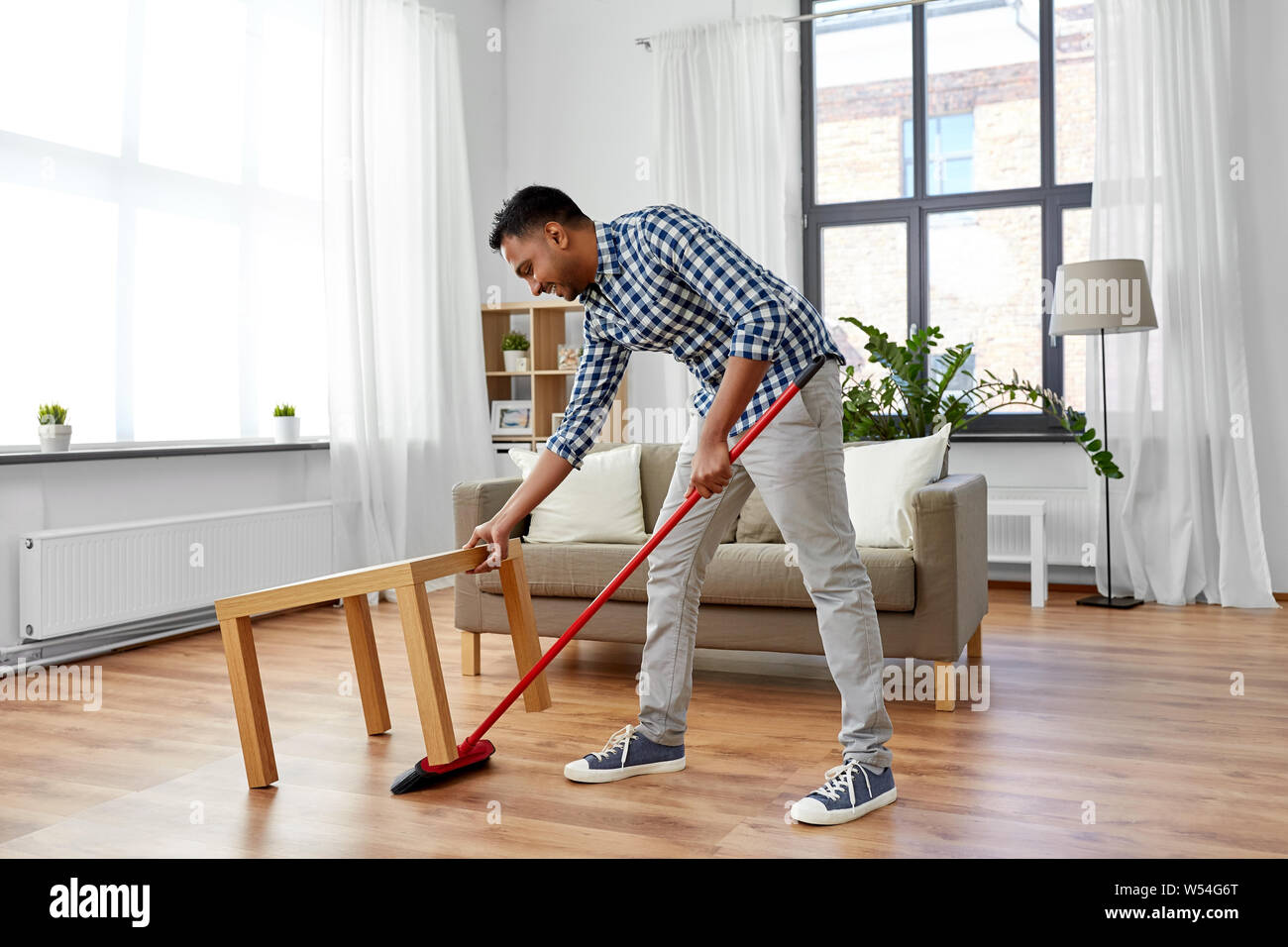 man with broom cleaning floor under table at home Stock Photo