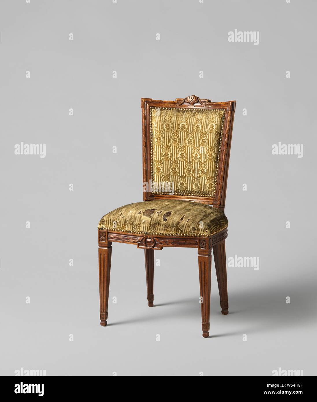 Armchair made of mahogany, covered with string with a continuous pattern of oval hanging flowers in which a flower on striped ground, covered with string with a continuous pattern of oval hanging flowers with a flower on it a striped ground. The square legs are fluted. The front line is decorated in the middle with a laurel wreath and a pendulum. The back frame is parallelogram-shaped and concave. The upper threshold is decorated with a stabbed vase and laurel garland. The cover is attached with nails with gold-plated heads. The chair belongs to an ameublement, anonymous, Northern Netherlands Stock Photo